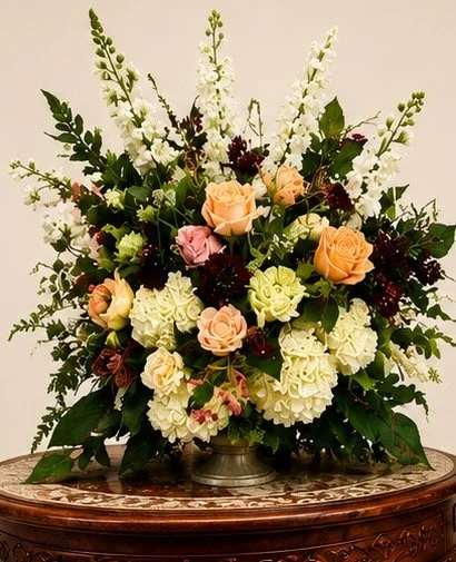 Elegant floral arrangement with white, pink, peach roses, and greenery on a wooden table.