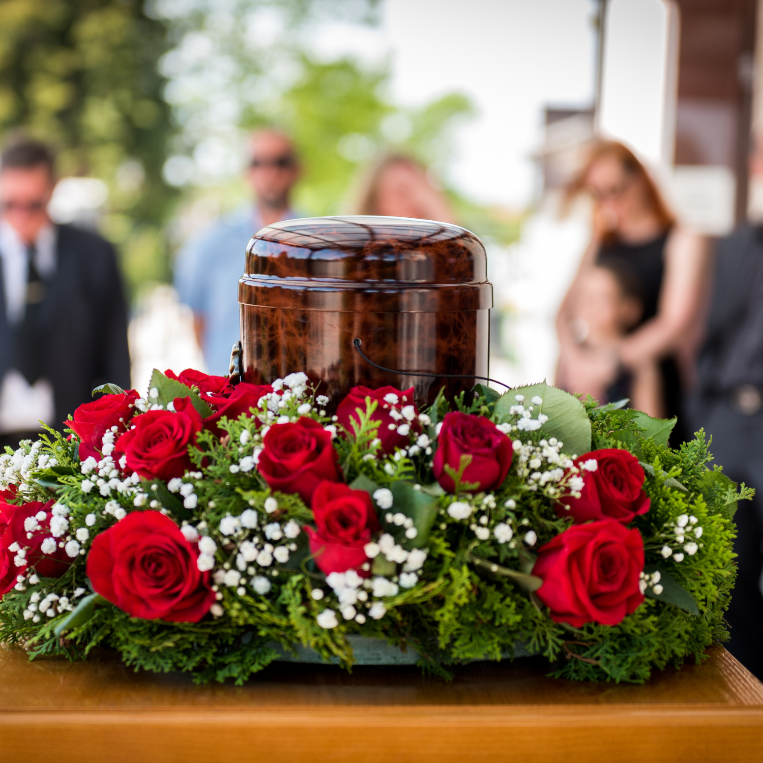 Red roses with greens and baby breath encircling an urn at a funeral