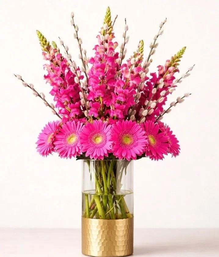 Modern gerbera arrangement with pink blooms and stock in a glass vase with gold base. by Gifts of Flowers TA