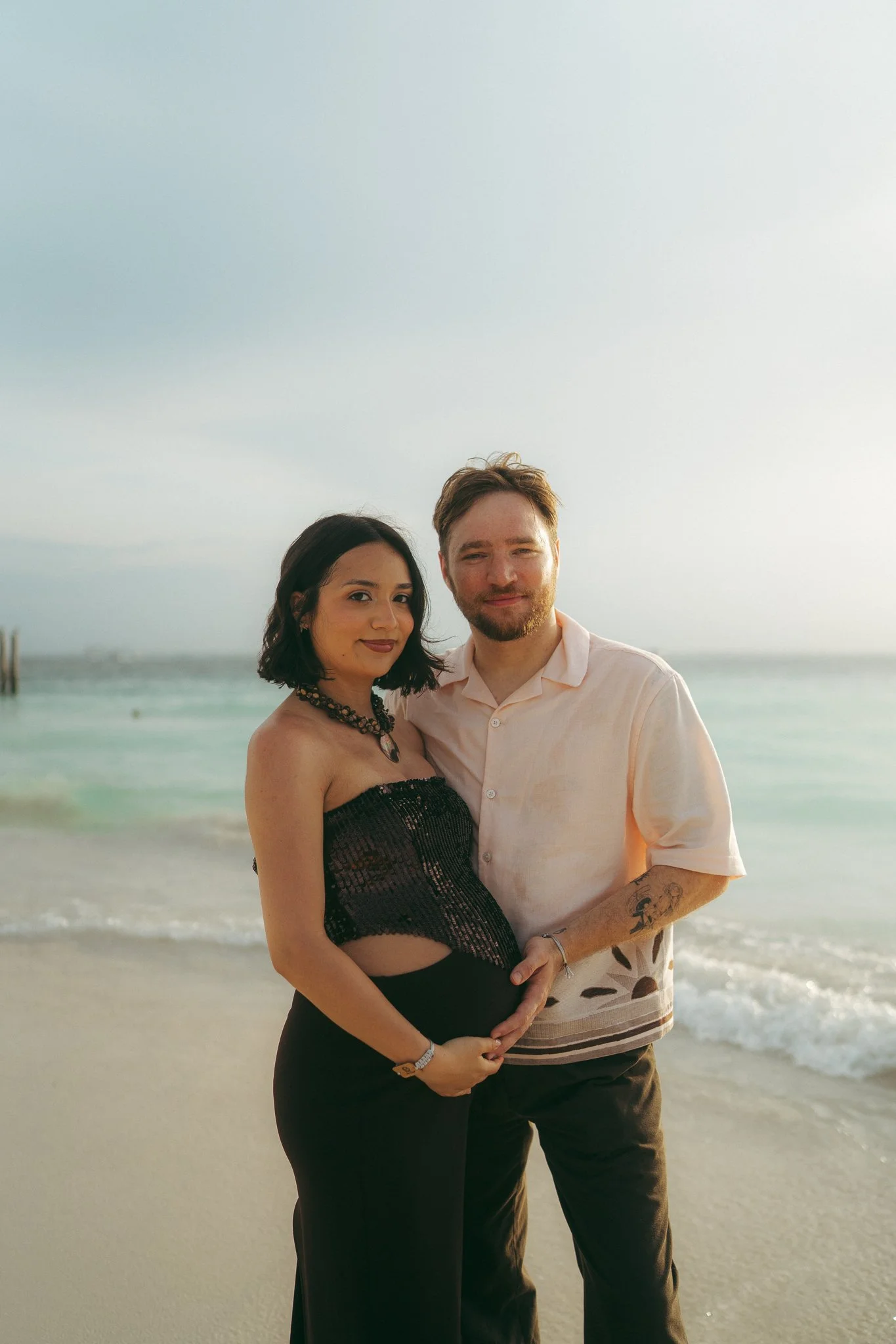 Pareja en la playa, con la mujer embarazada, disfrutando del atardecer.
