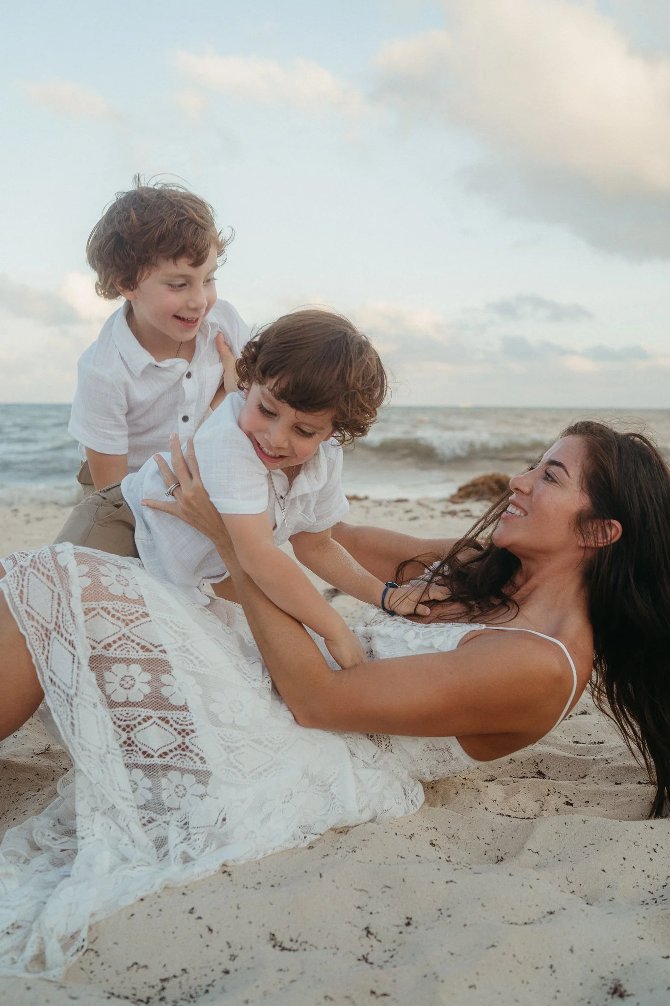 Mujer y dos niños jugando y divirtiéndose en la playa, acostados sobre la arena cerca del mar.