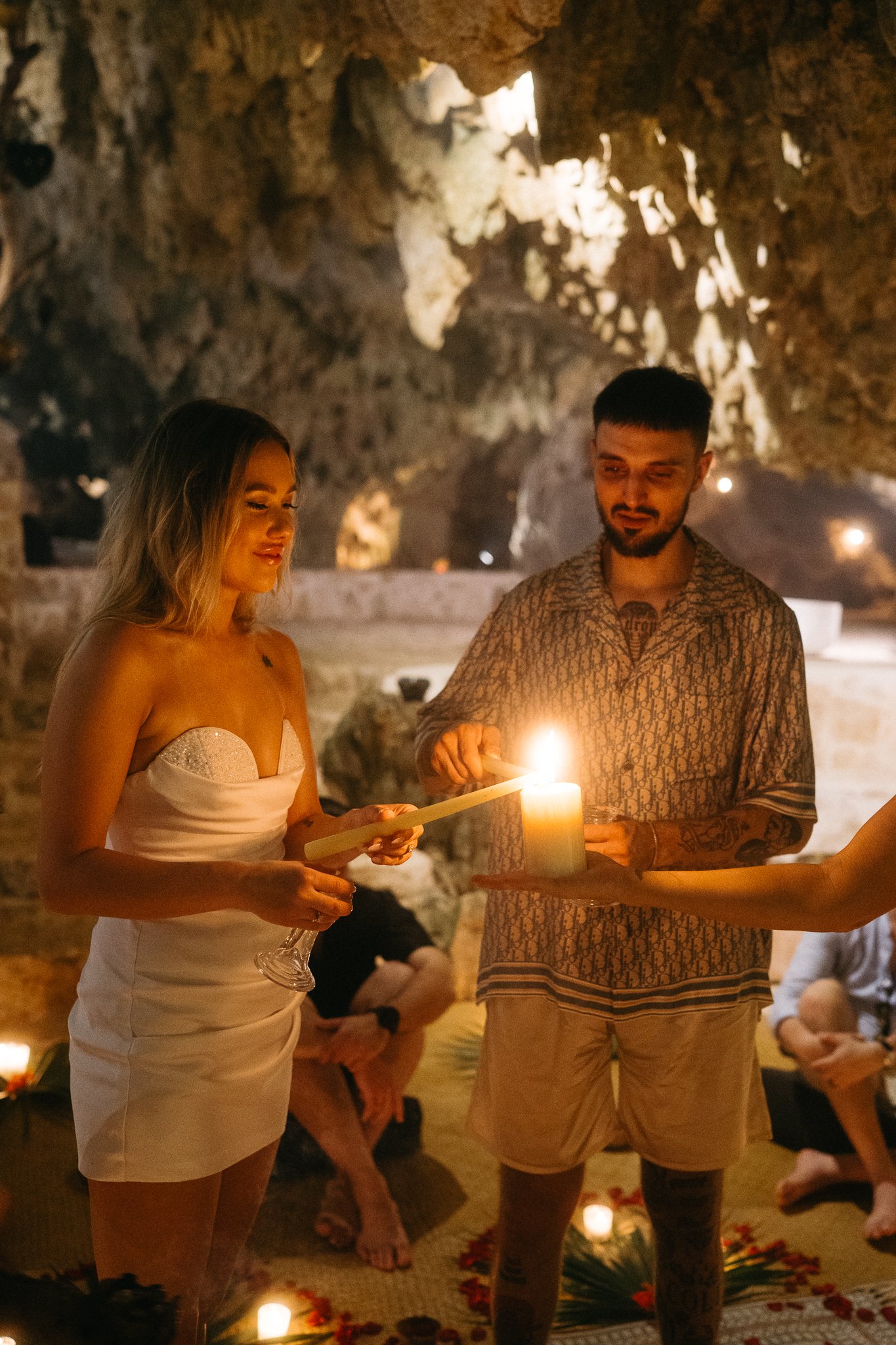 Muchas personas participando en una ceremonia en una cueva, encendiendo una vela y leyendo de un pergamino, con luz cálida y ambiente místico.