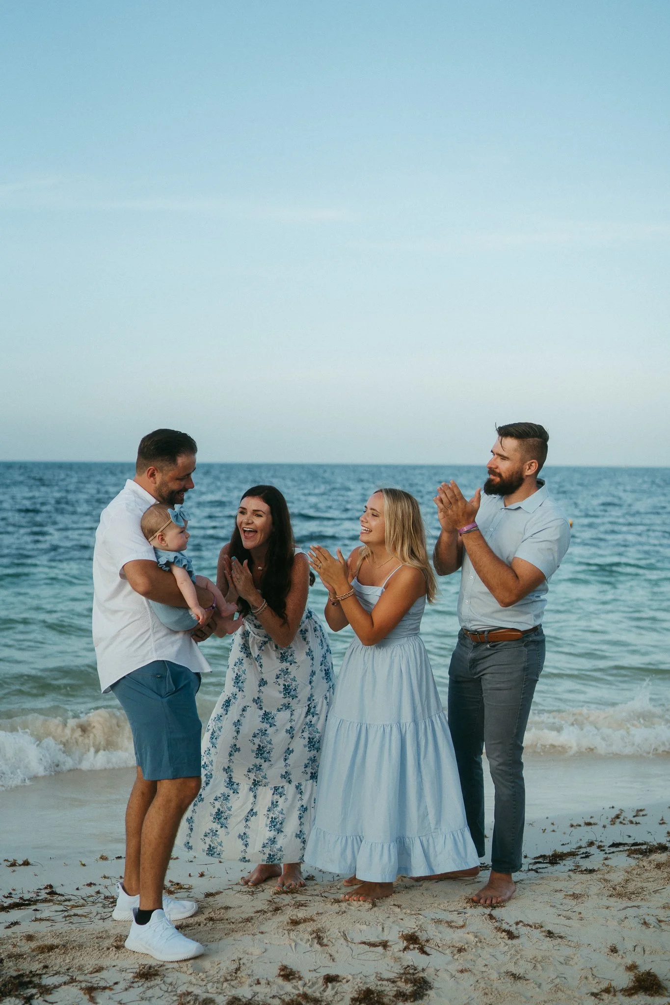 Familia en la playa celebrando, con el mar y cielo azul de fondo.