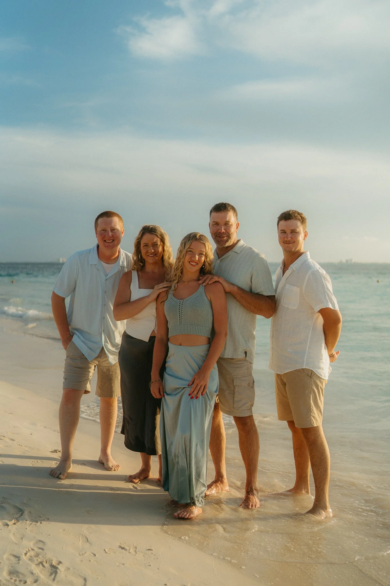 Grupo de seis personas sonriendo en la playa, con el mar y el cielo nublado de fondo.