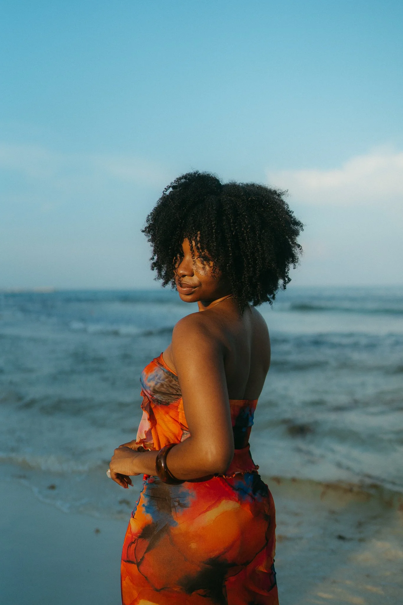 Mujer con vestido colorido en la playa con el mar y el cielo de fondo.