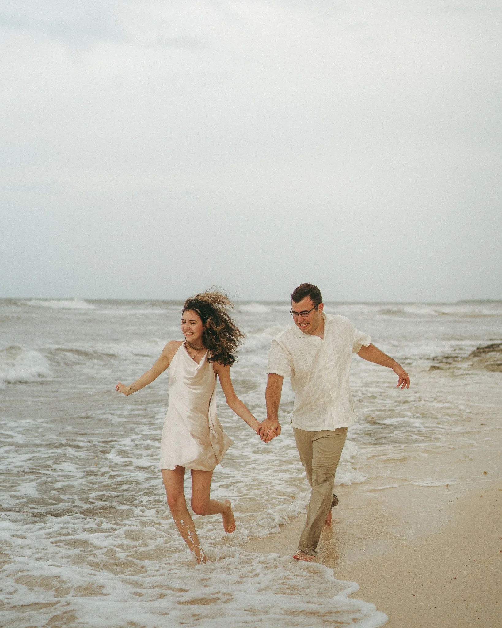 Una pareja feliz corre y se divierte en la orilla del mar en un día nublado.