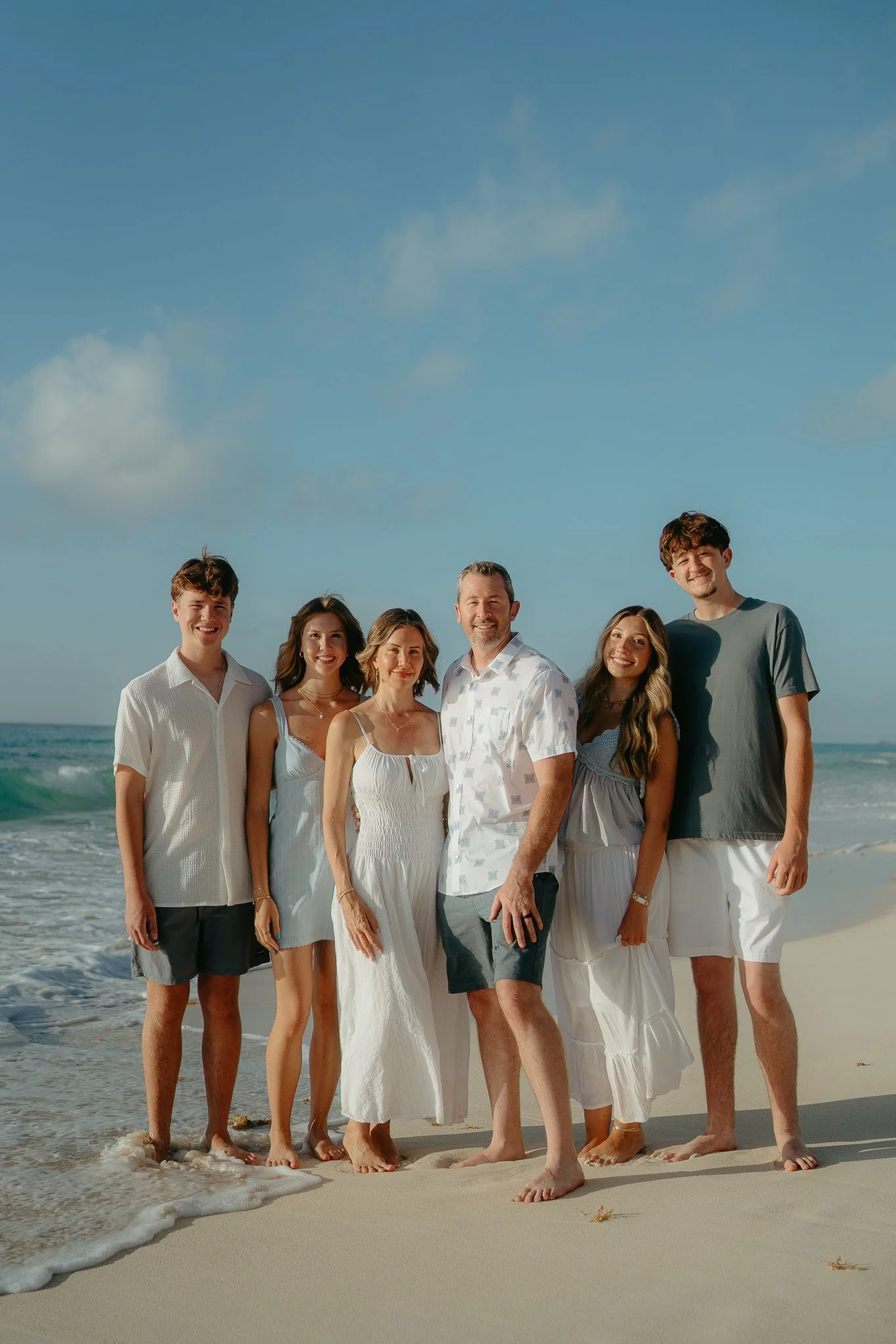 Grupo de seis personas en la playa, sonríen y posan para la cámara con el mar y el cielo de fondo.