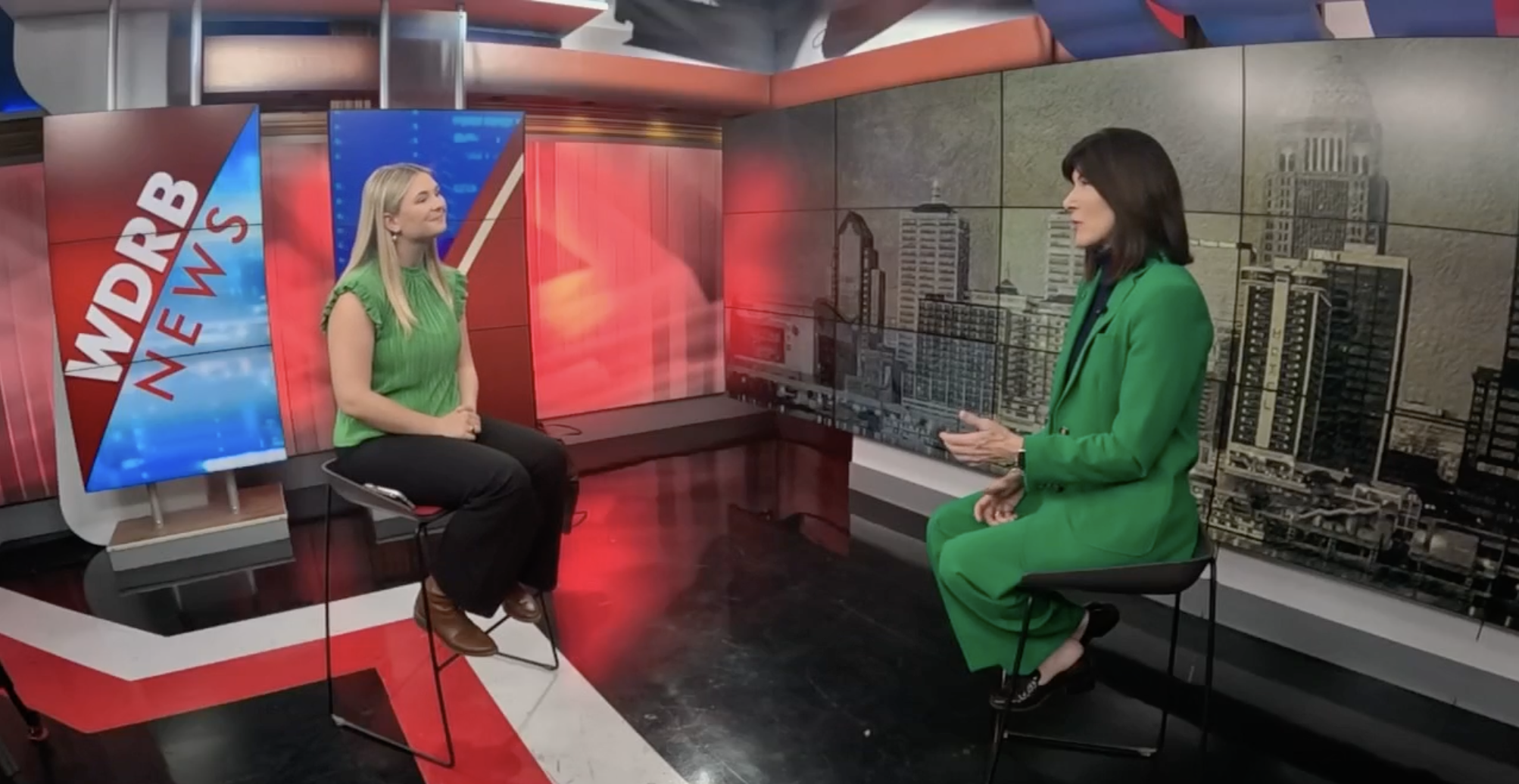 Two women are having a conversation on a television news set with a WDRB News logo, featuring a city skyline background.