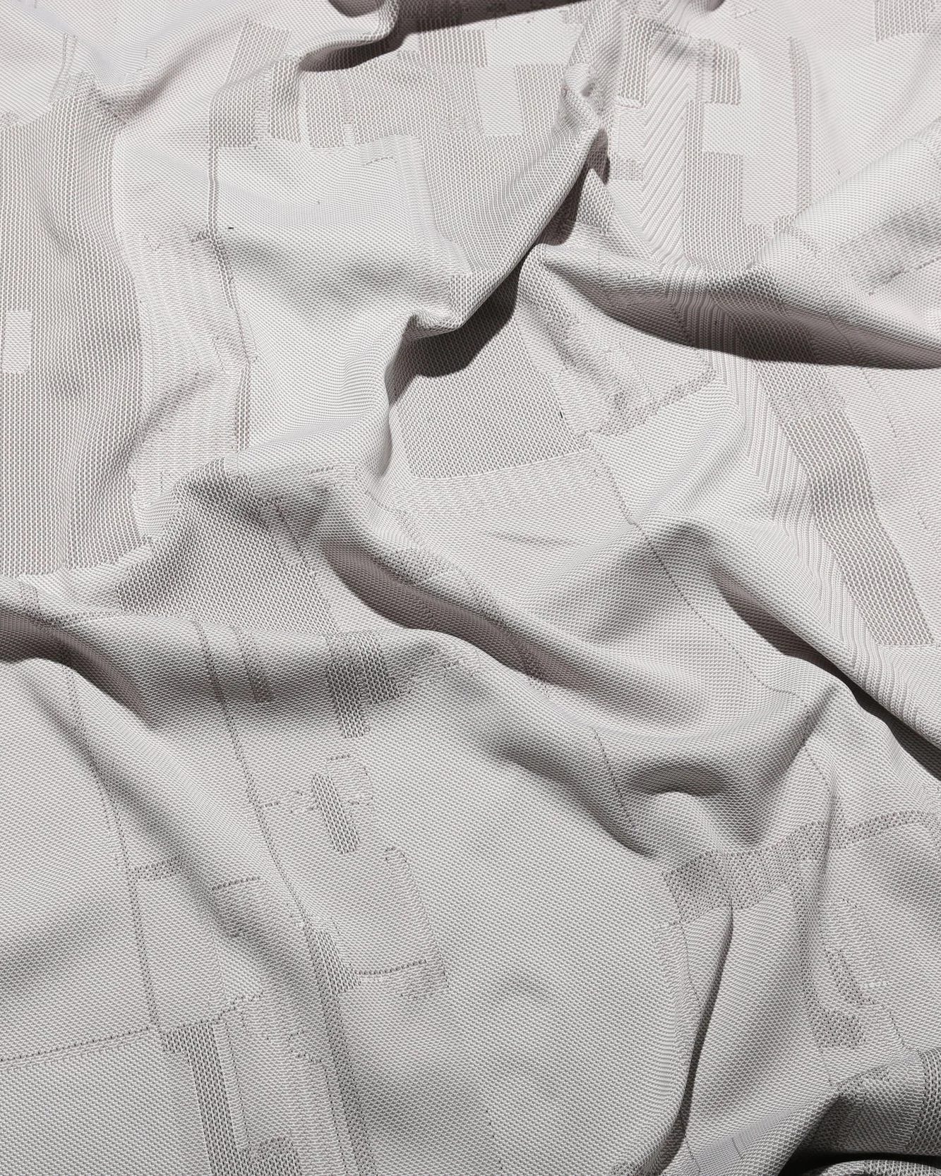 Draped knit fabric in pale grey with a subtle tonal geometric pattern. Byborre Edition textile.