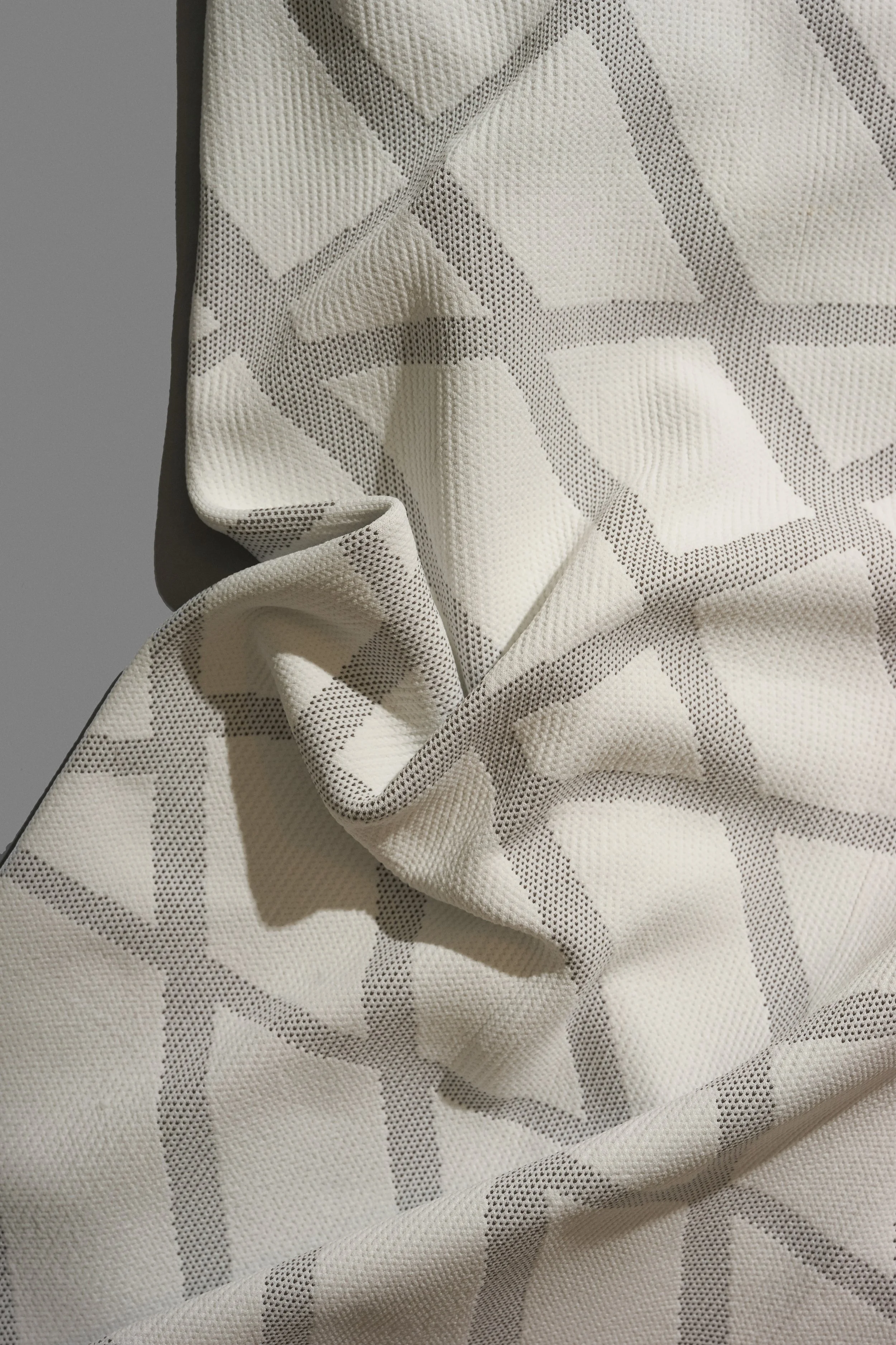 Draped knit fabric in off-white with allover Adidas logo pattern in grey. Textile development by Byborre for Adidas.