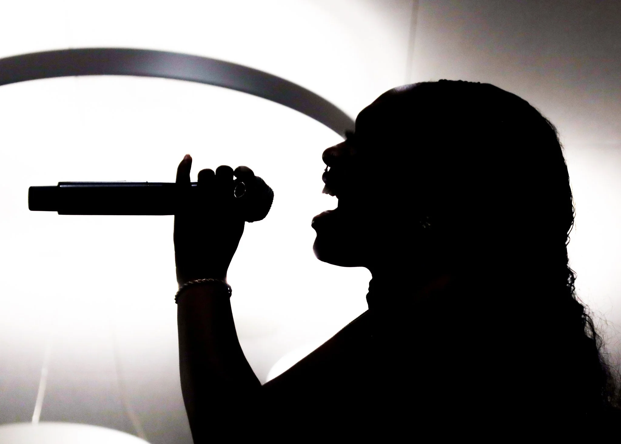 Silhouette of a woman singing into a microphone, with a bright light behind her.