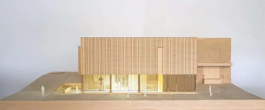 Architectural model of a modern building with vertical wooden slats, large glass windows, and small figurines of people in front.