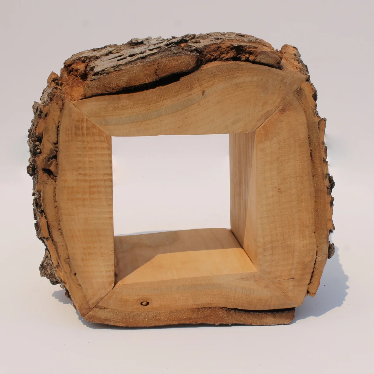 A wooden square frame with bark on the outside, made from a cross-section of a tree trunk, showing the inner smooth wood and outer rough bark.