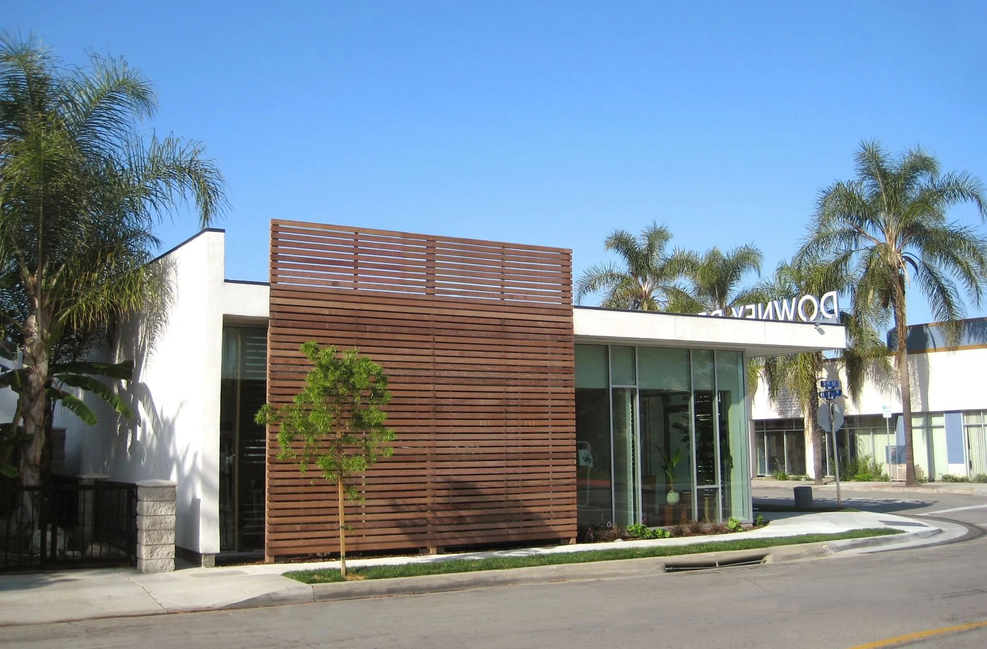 Modern building with a wooden slat facade, glass entrance, and palm trees in the background on a sunny day.