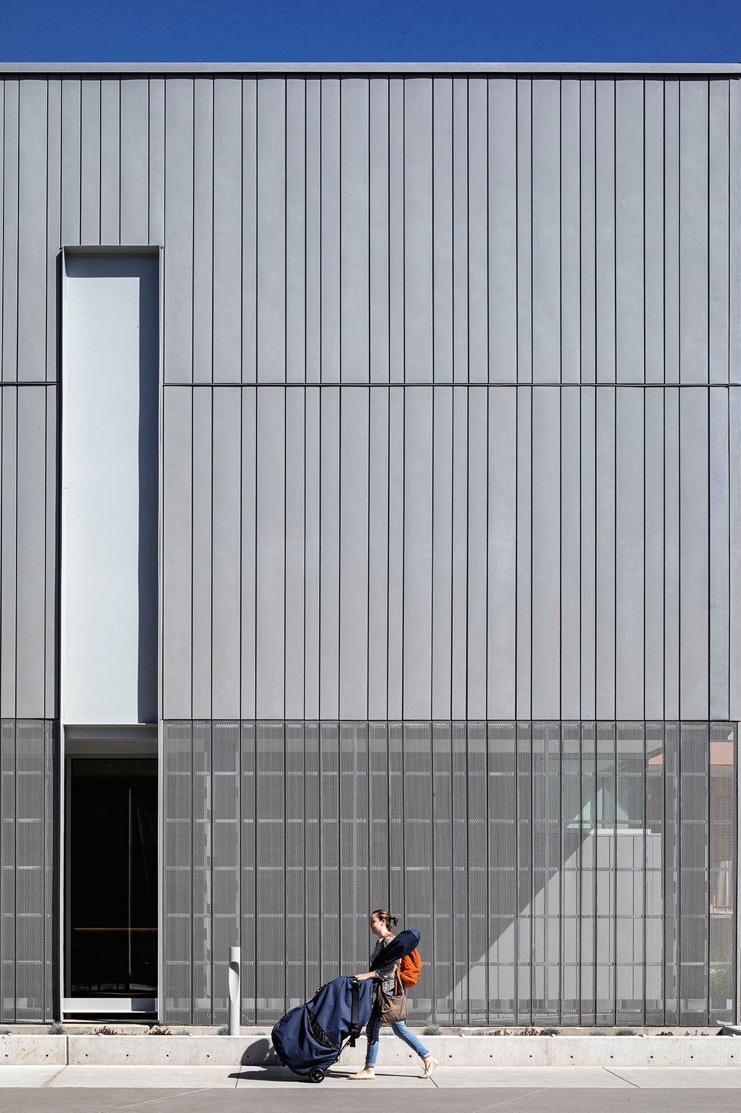 Woman rolling cello in front of modern steel facade and vertical window designed by Sparano + Mooney Architecture