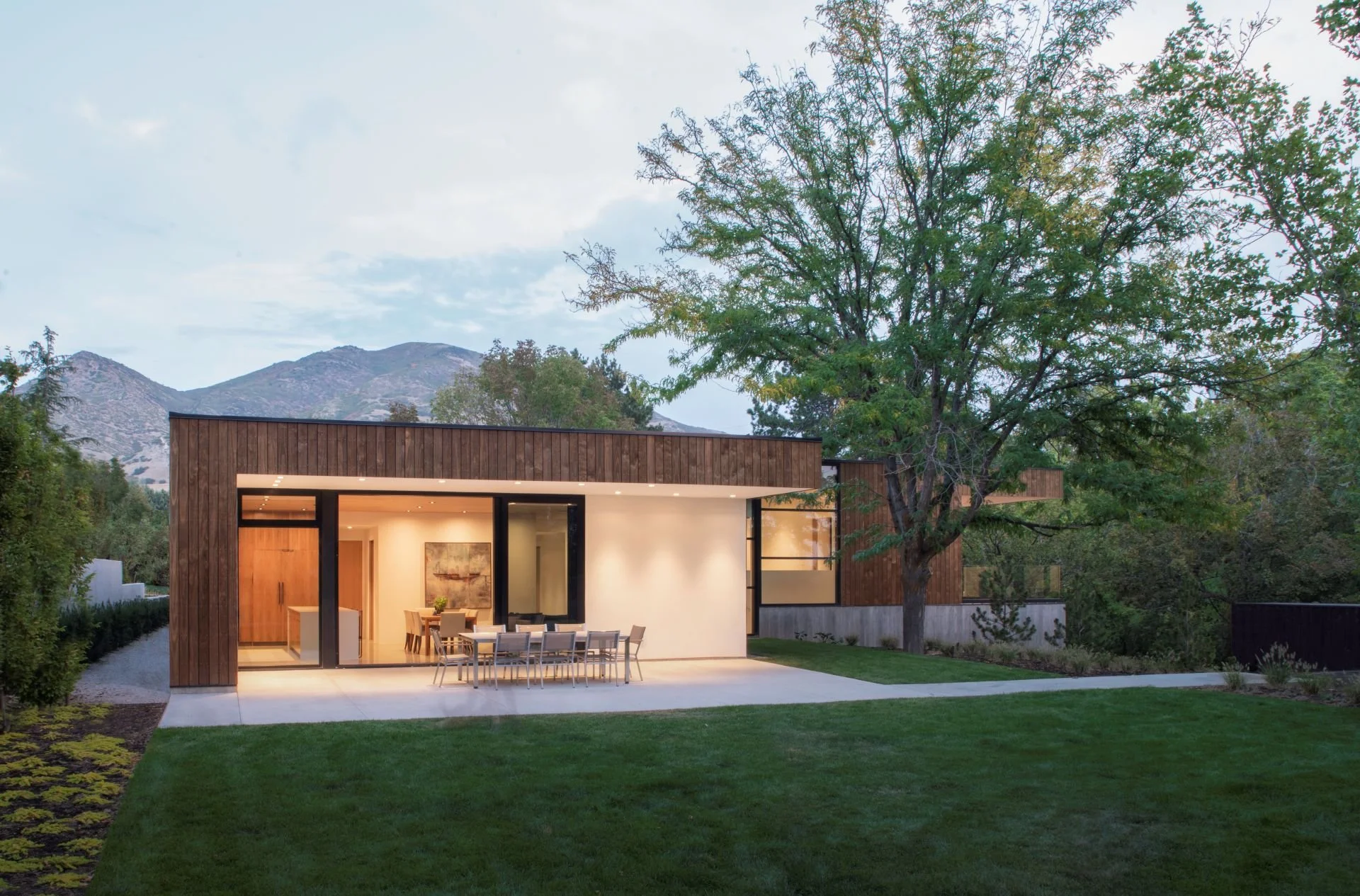 Night perspective of back patio with illuminating interior and Wasatch mountains designed by Sparano + Mooney Architecture