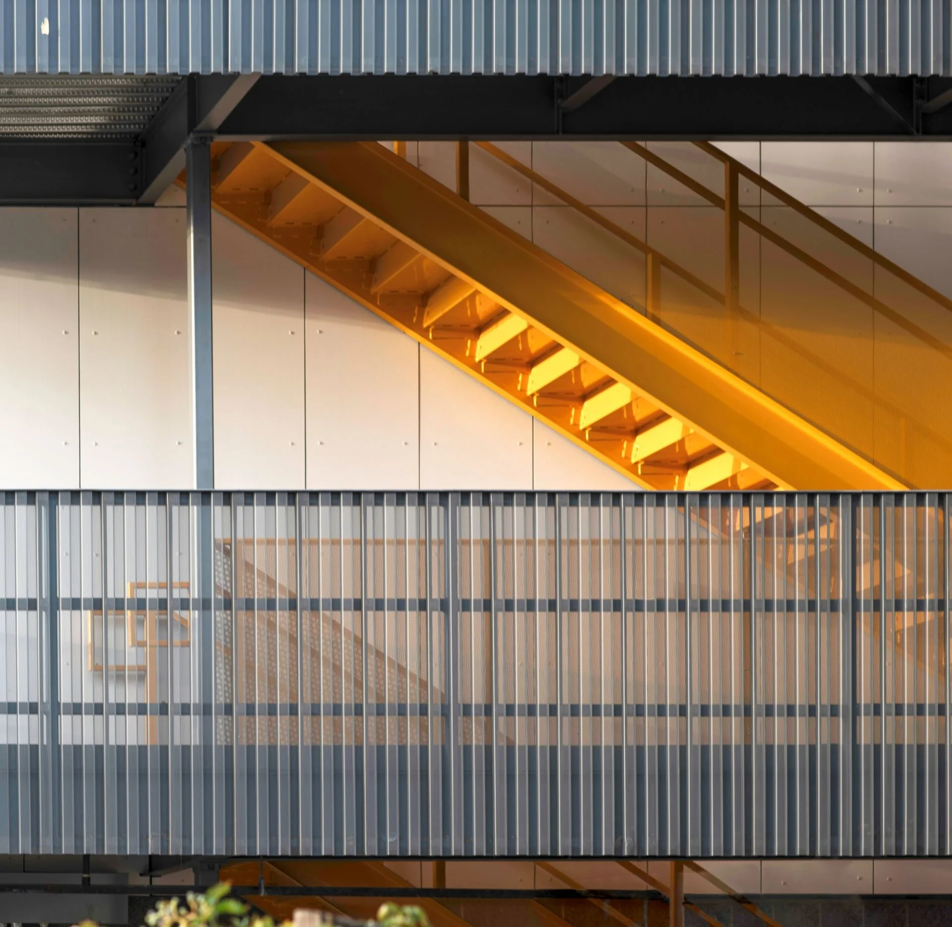 Modern building exterior with yellow staircase, metal railing, and beige wall panels.