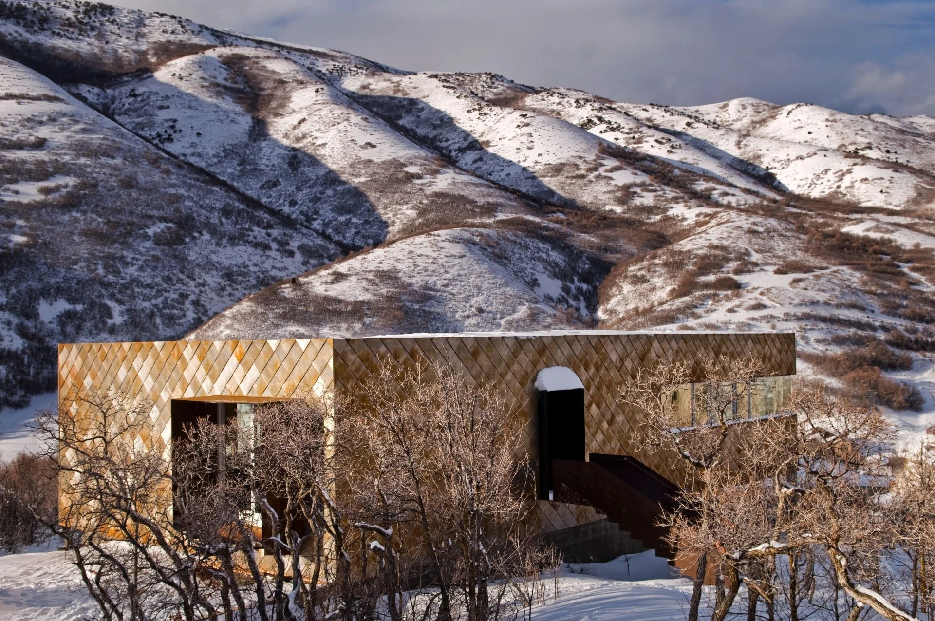 Modern corten steel house in Salt Lake City by Sparano + Mooney Architecture amid snowy mountains.