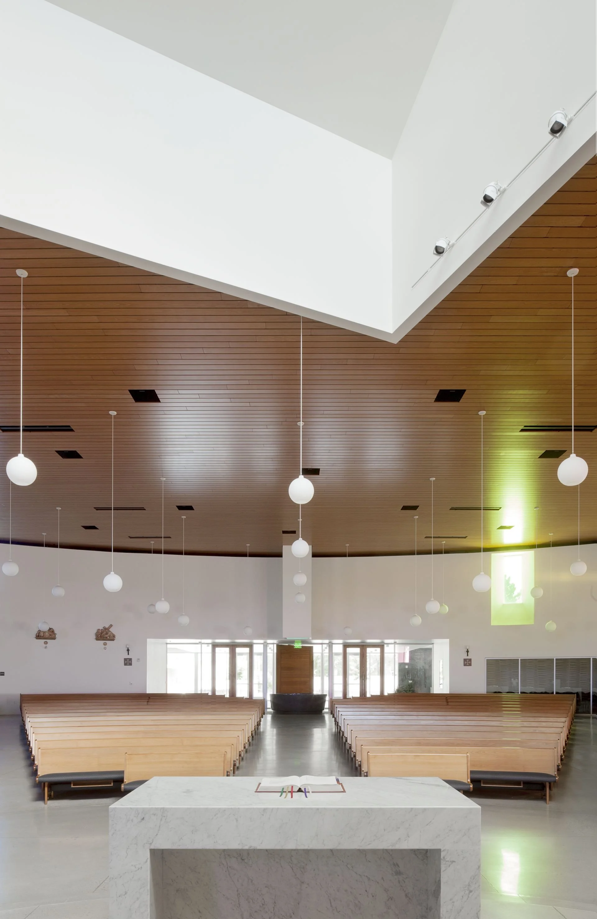 View from marble altar of wooden pews with wood ceiling and spherical pendant lights designed by Sparano + Mooney Architecture