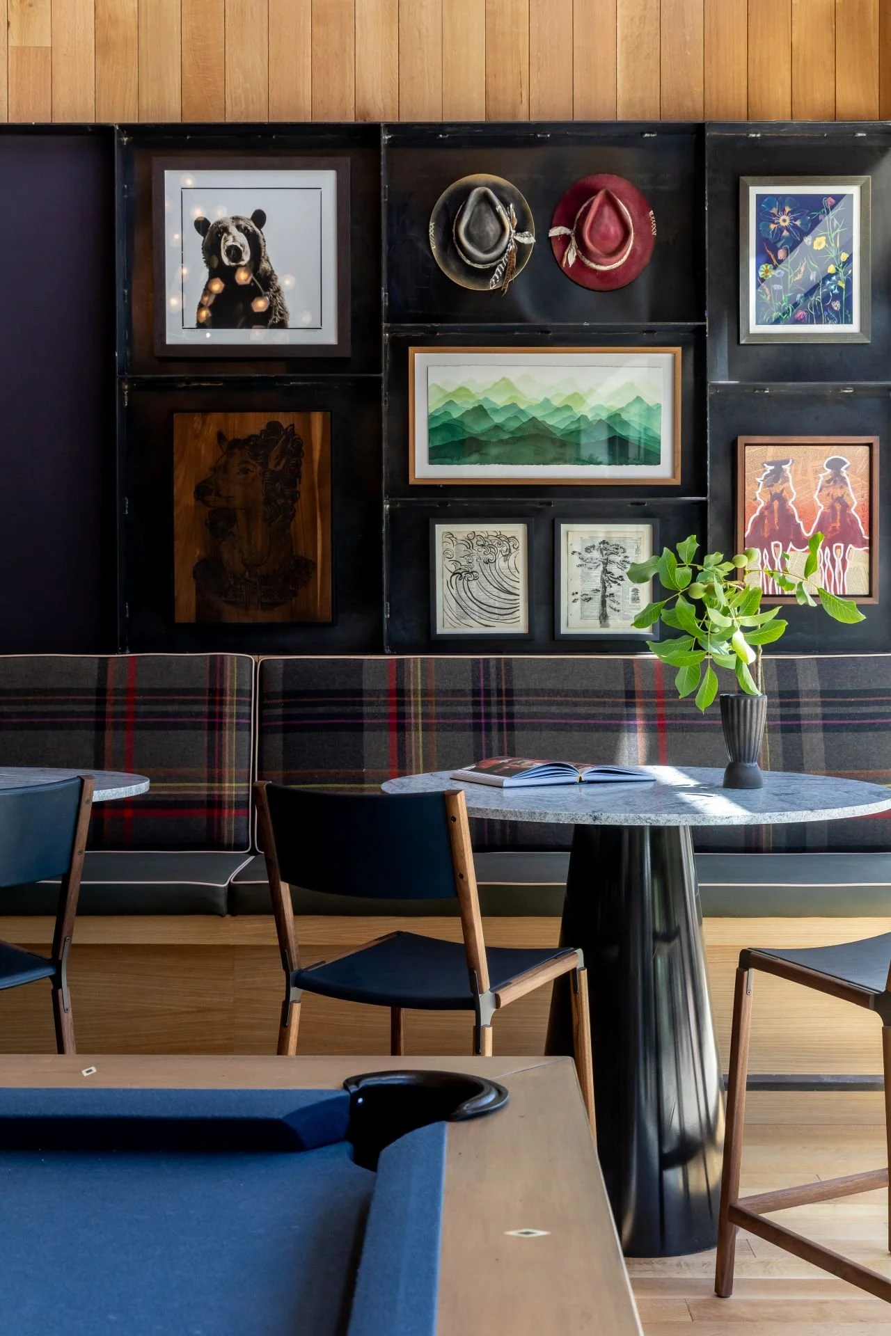 Cafe interior with wall art, wooden furniture, a marble table with a potted plant, and a pool table in the foreground.