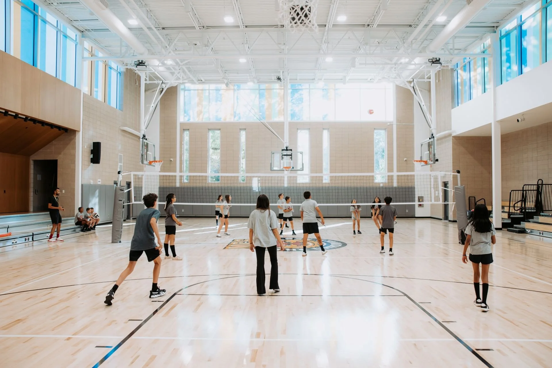Children playing volleyball in bright gym with colorful glass facade designed by Sparano + Mooney Architecture
