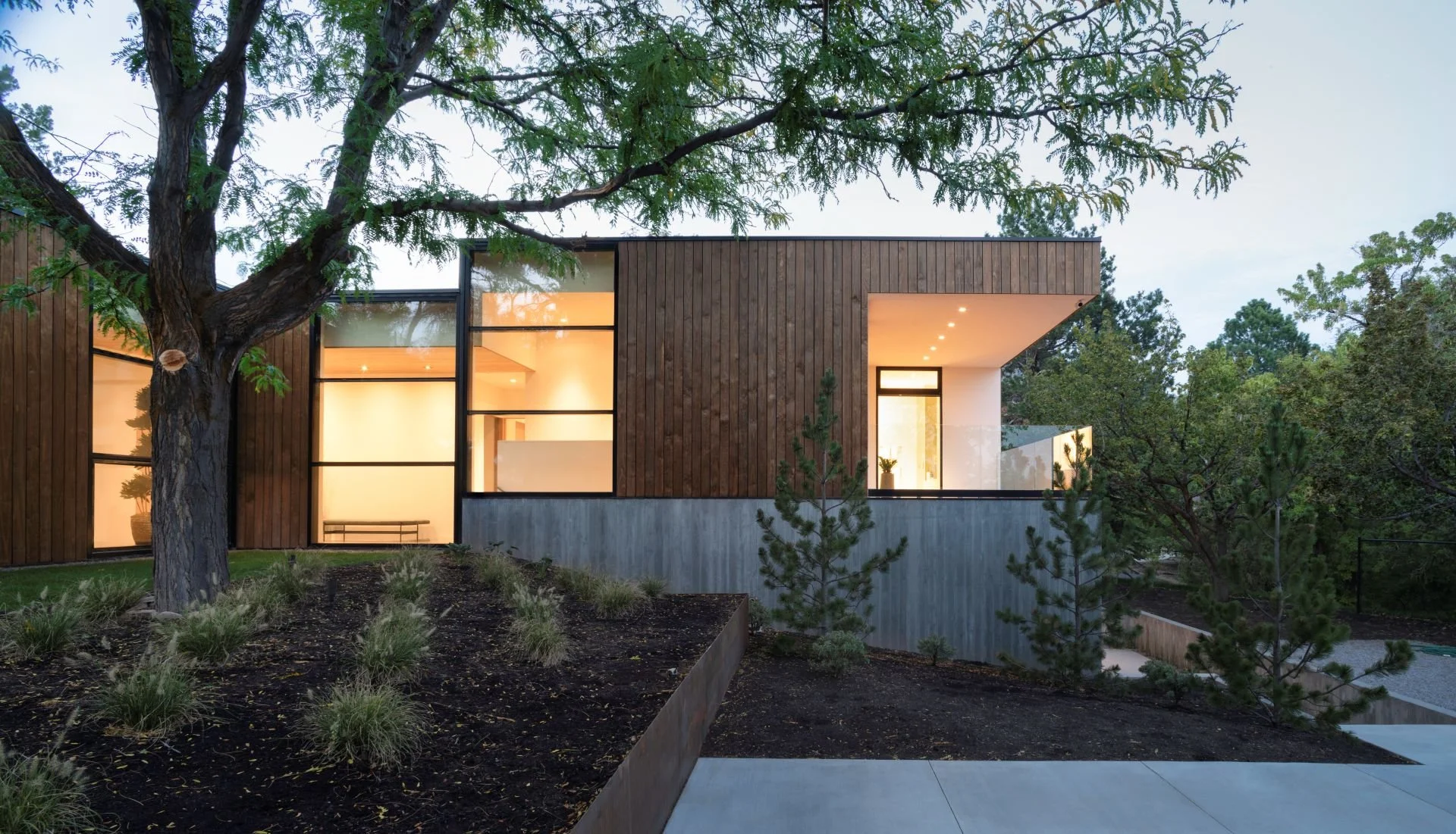Night side elevation view with illuminating interior through large glass facade and landscaped yard designed by Sparano + Mooney Architecture