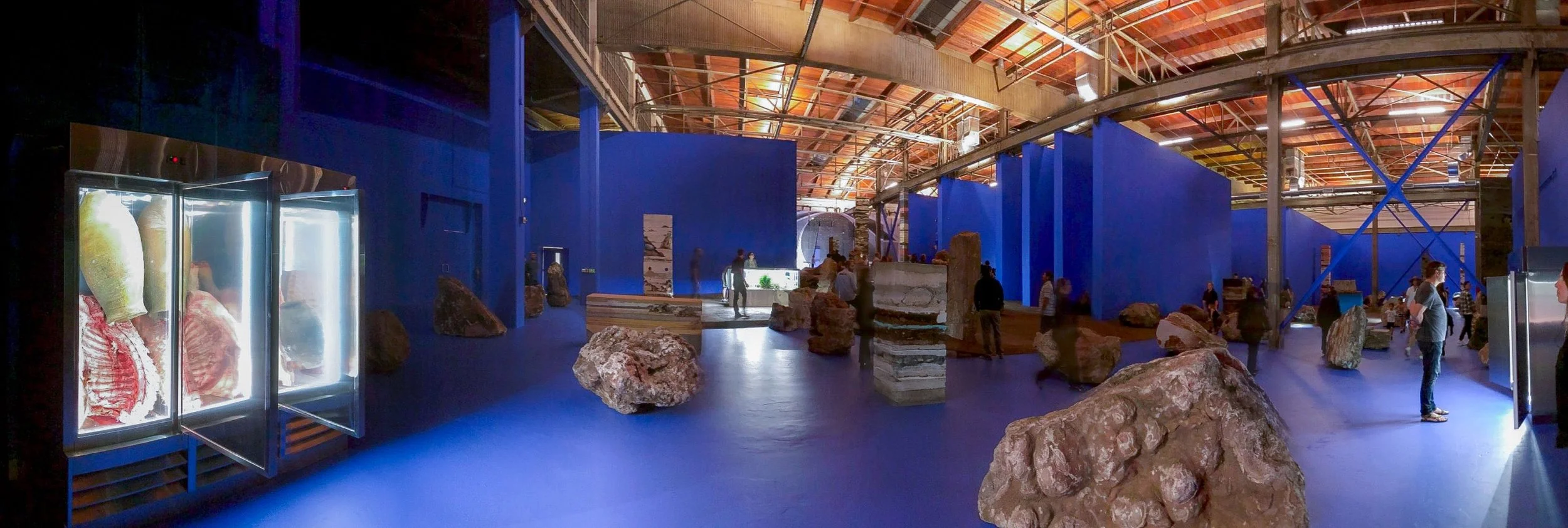 Wide lens view of Adrian Villar Rojas MoCA installation with blue walls and scattered boulders designed by Sparano + Mooney Architecture