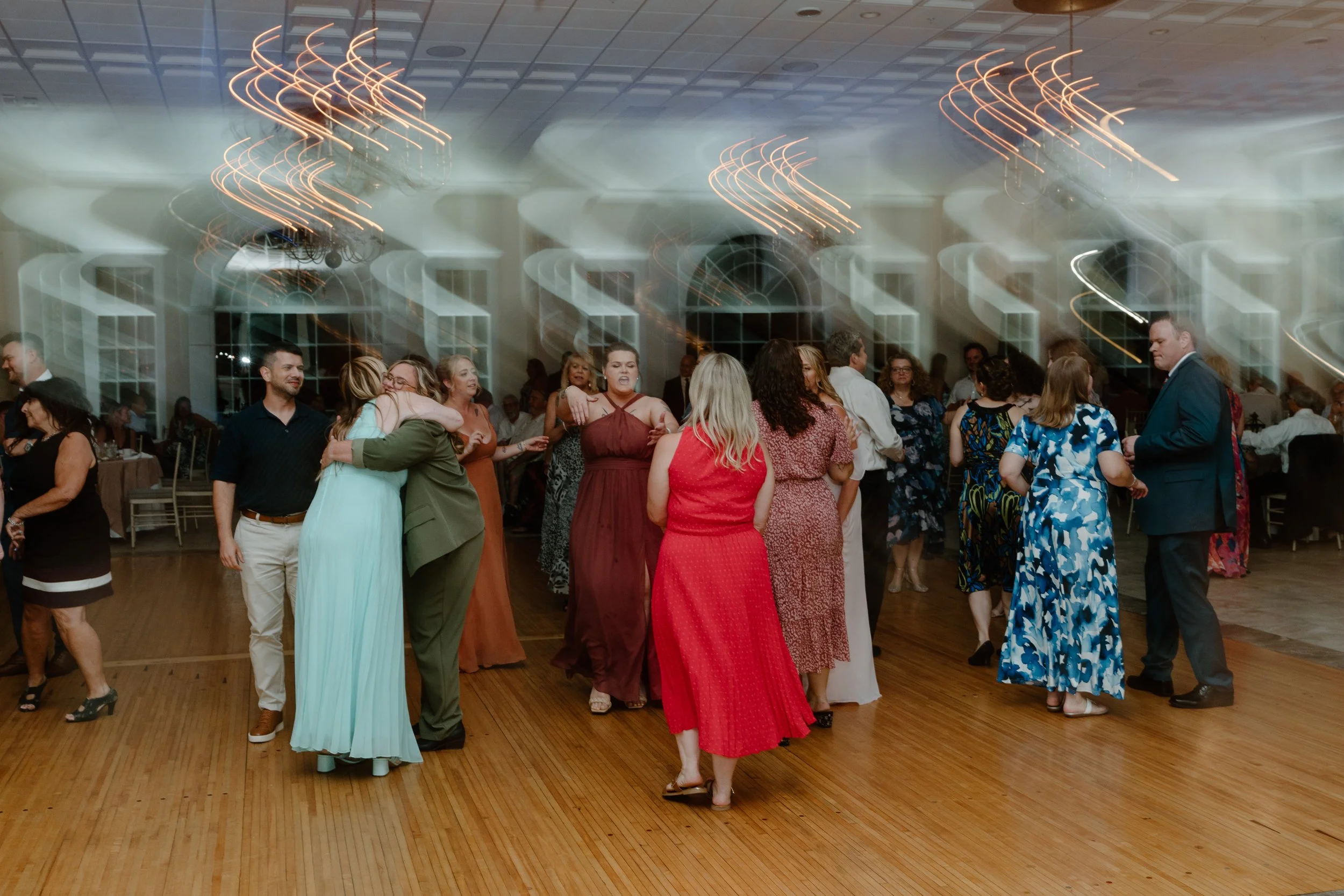 People dancing and socializing at a lively indoor event with colorful attire and motion blur lights overhead during a wedding at the Aqua Turf Club in Connecticut. 