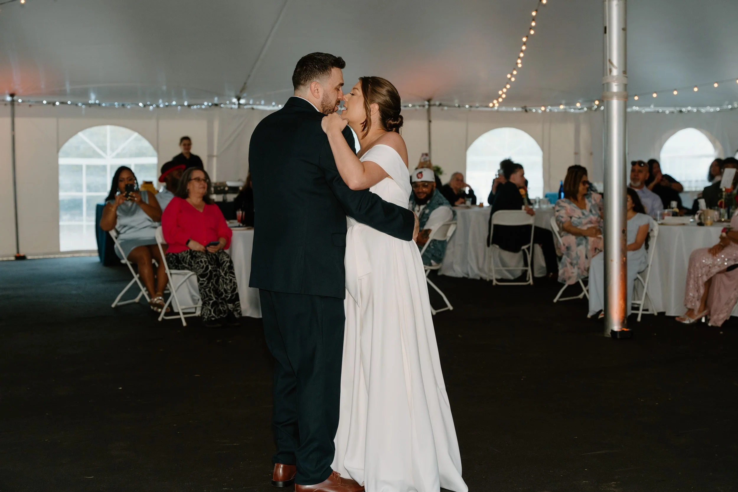 A bride and groom share a dance at their wedding reception inside a decorated tent, with guests seated at tables in the background for a wedding at Holiday Hill Day Camp in Connecticut.