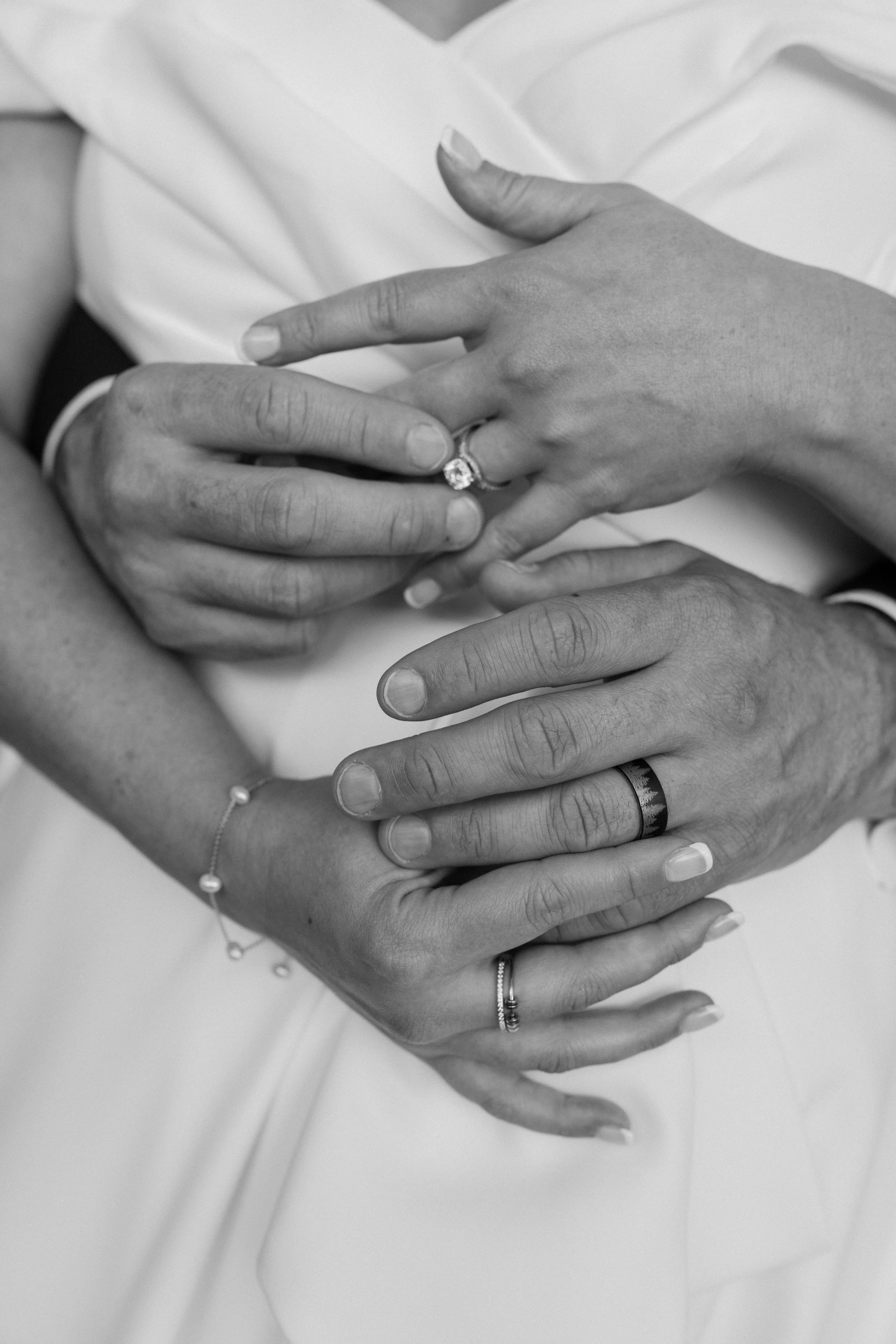 Close-up of a person’s hands with wedding rings, embracing another person’s hand, also wearing a ring and jewelry, all in black and white for a wedding at Holiday Hill Day Camp in Connecticut.