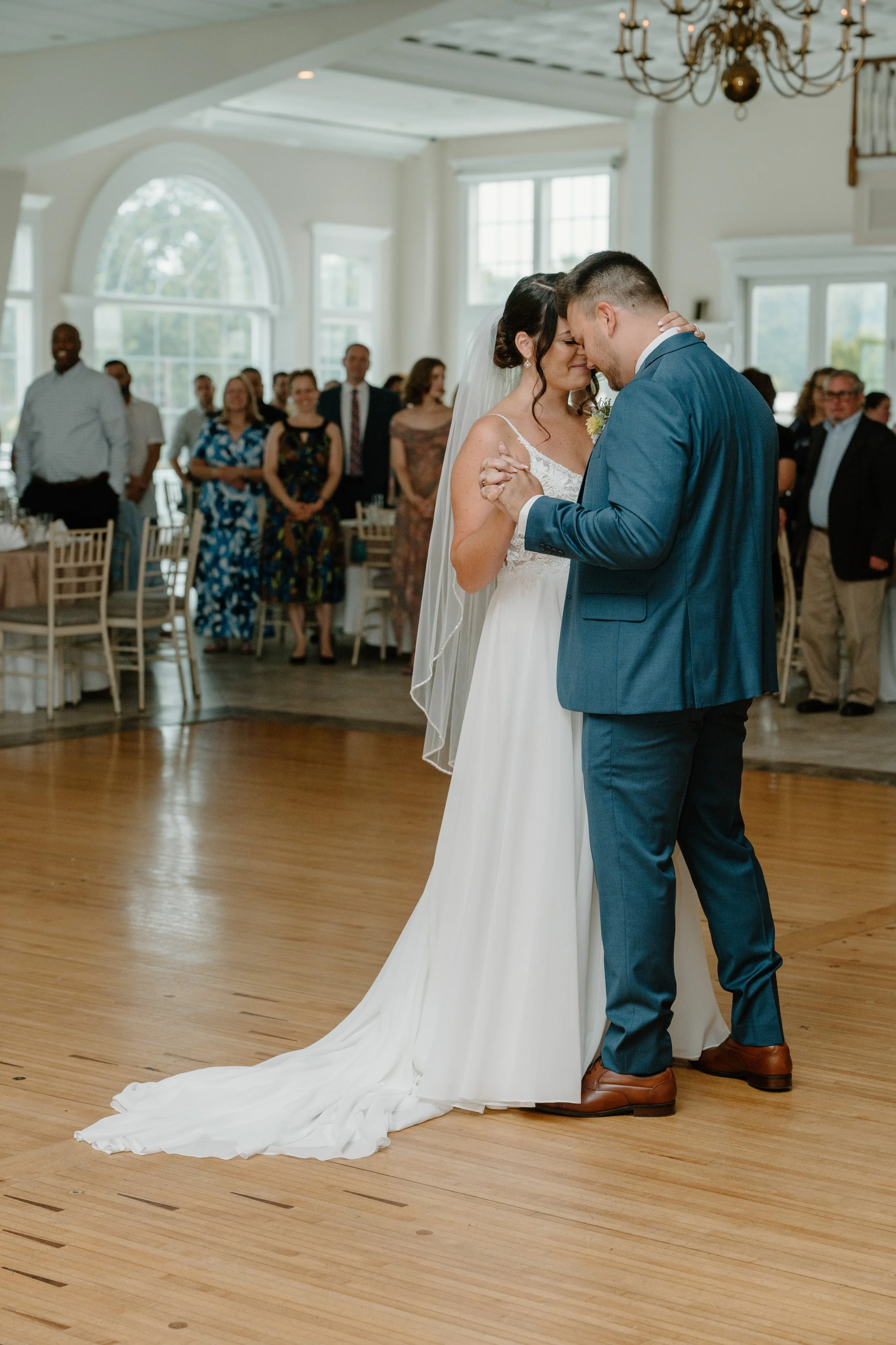 A bride and groom share their first dance at a wedding reception, with guests watching in the background inside a decorated venue during a wedding at the Aqua Turf Club in Connecticut. 