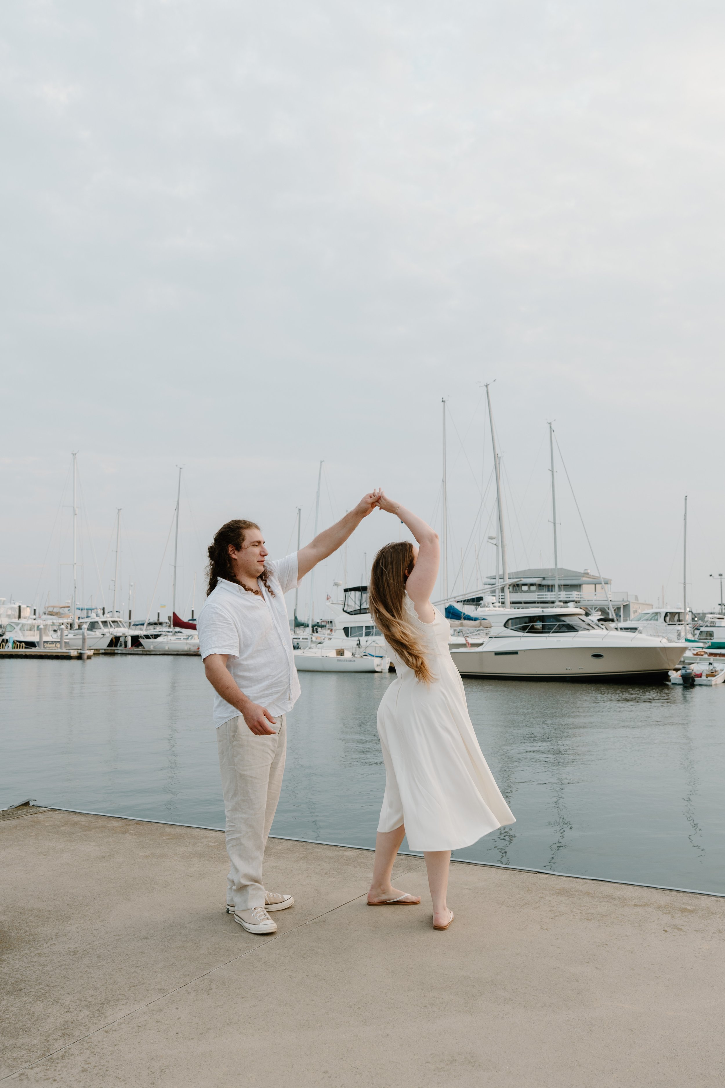 A couple dancing by a marina with sailboats in the background after an elopement at Beavertail State Park in Rhode Island. 