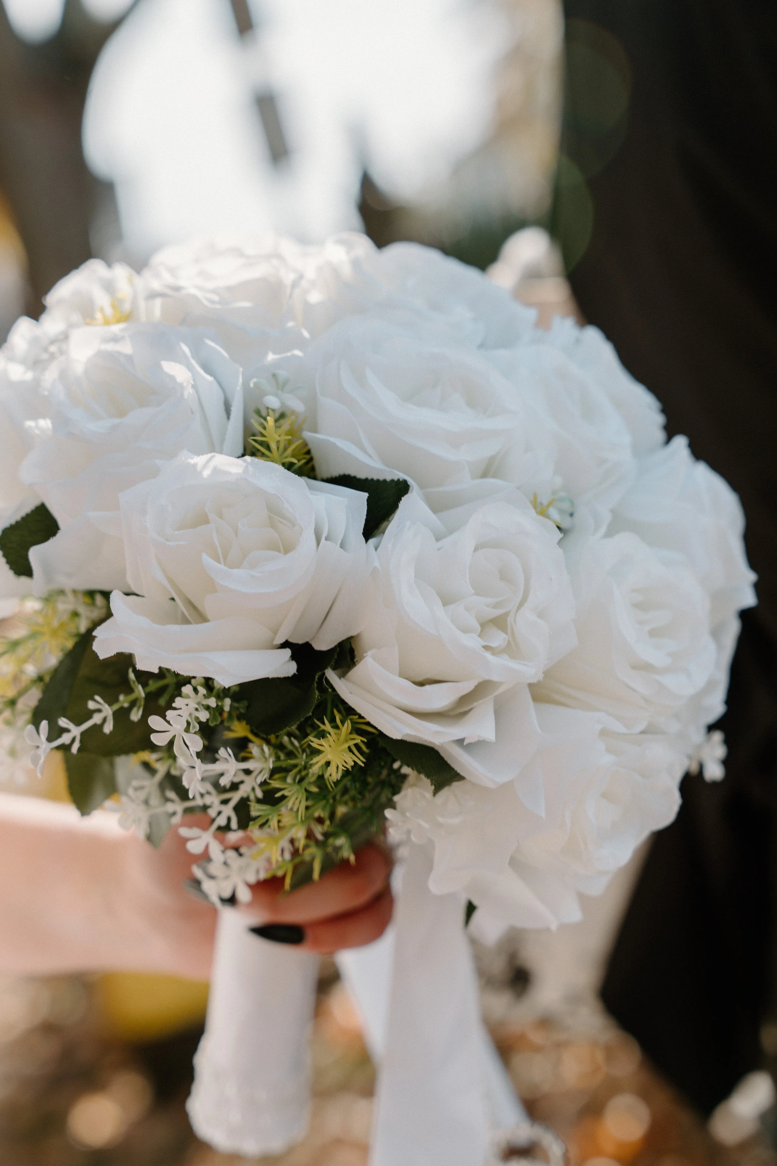 A bouquet of white roses being held by a person with black nail polish.