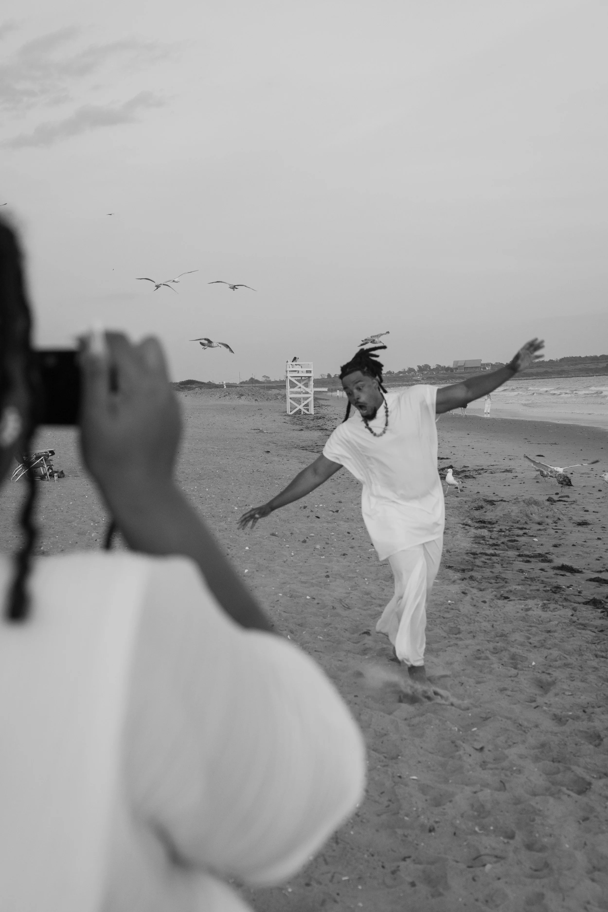 A person wearing white clothing dancing on the beach as another person takes a photo at an elopement at Second Beach in Rhode Island. 