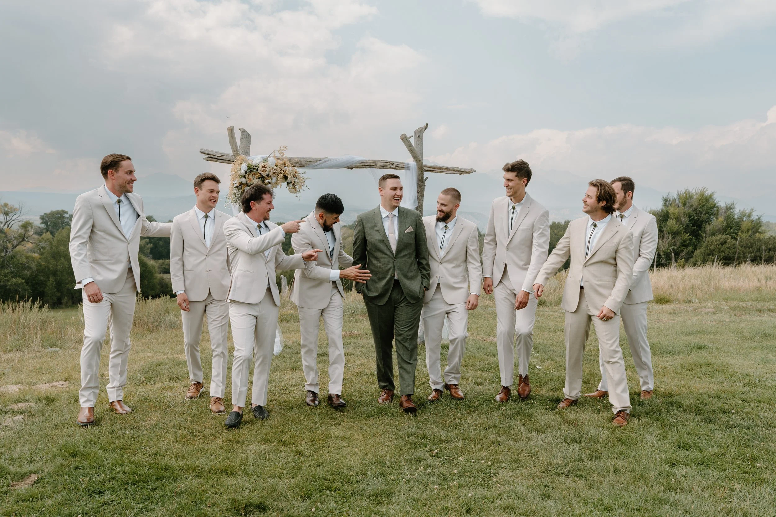 A groom and groomsment in suits walking outdoors in a grassy field at a wedding at Everett Ranch in Salida, Colorado.