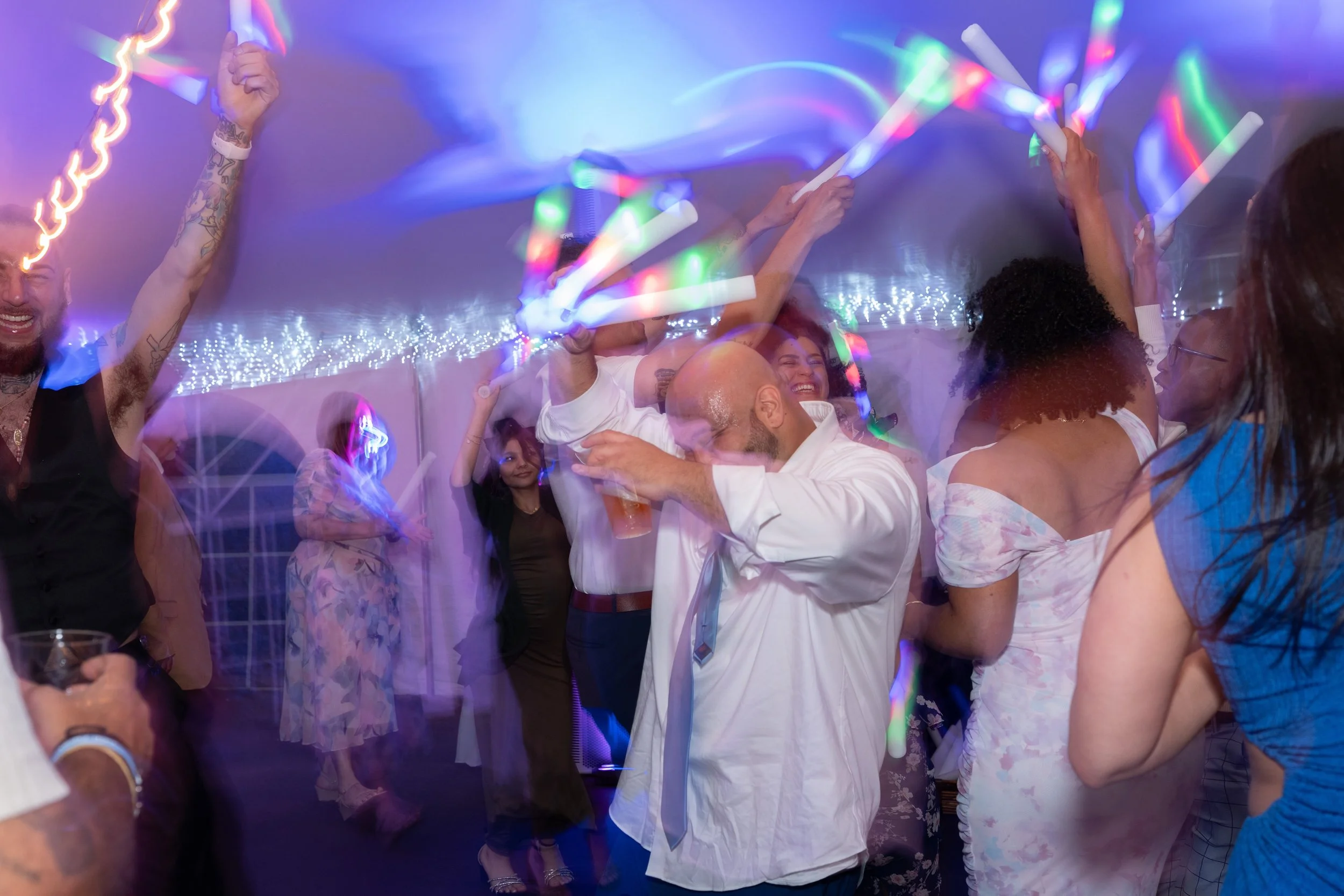 People dancing and celebrating at a party with colorful lights and glow sticks.