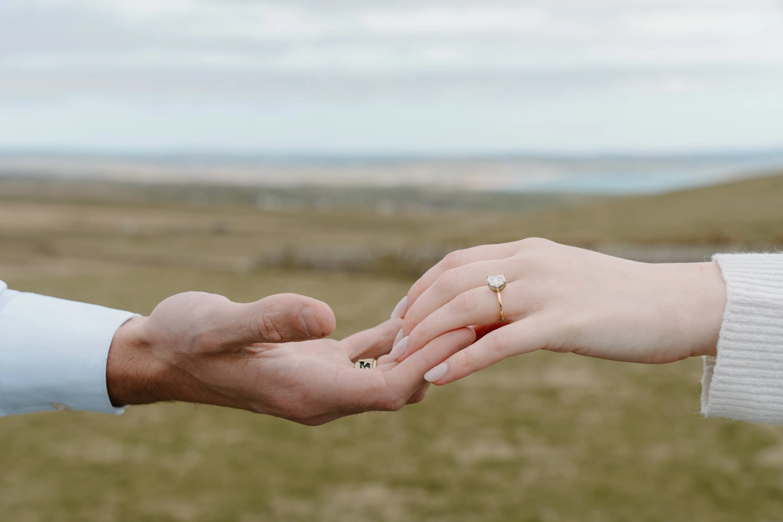 A couple holding hands outdoors, with one person wearing a wedding ring on their finger for an engagement photo session in Galway, Ireland. 