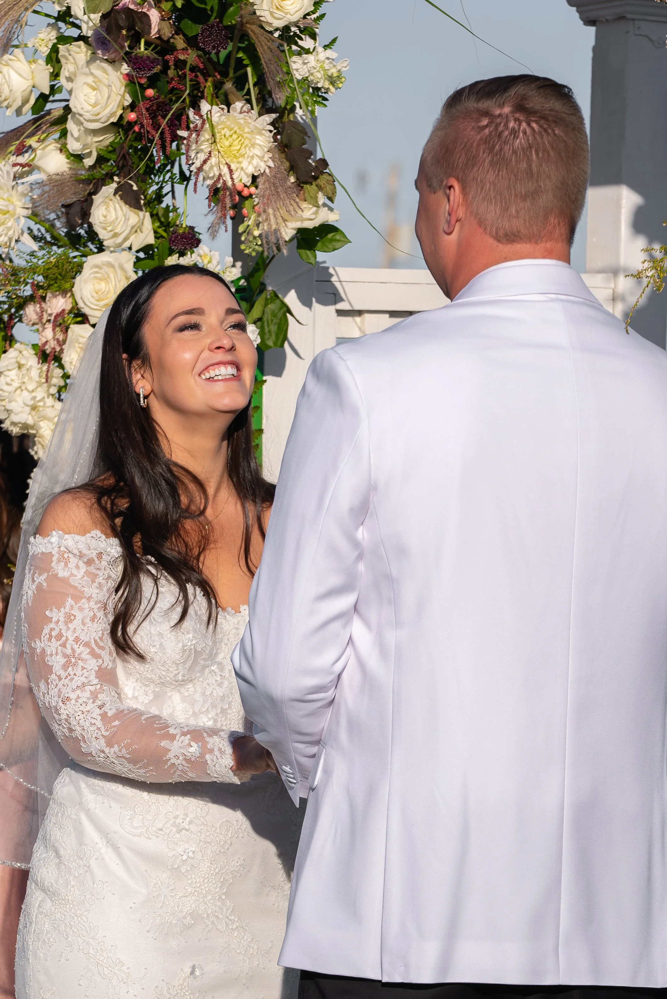 A bride with long dark hair and a lace wedding dress is smiling and looking at her groom during a wedding at Red Jacket Resort in Cape Cod. 
