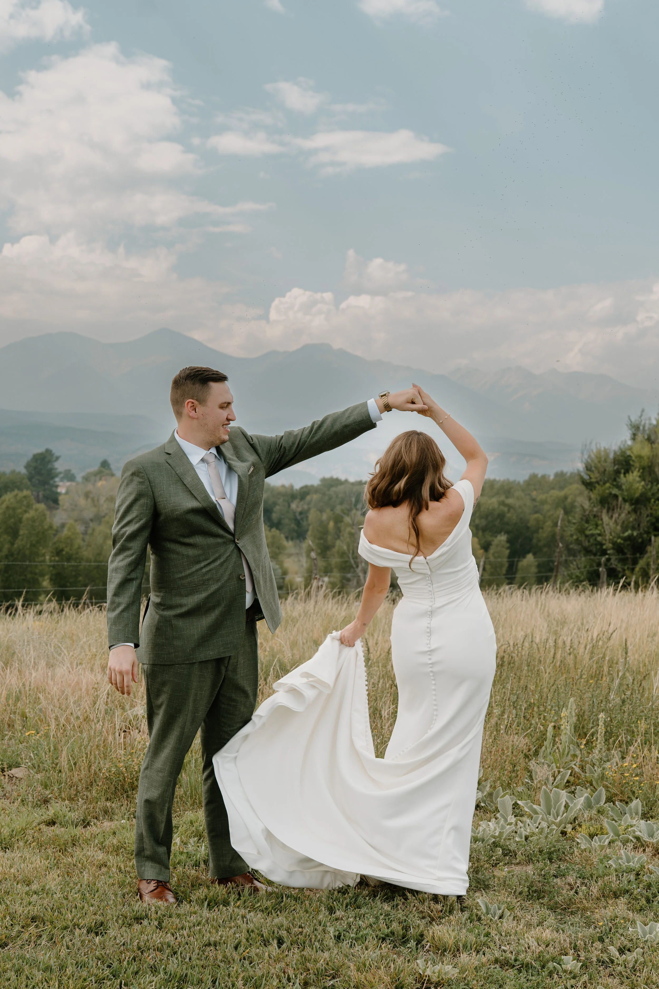 A bride and groom in a field with mountains in the background at a wedding at Everett Ranch in Salida, Colorado.
