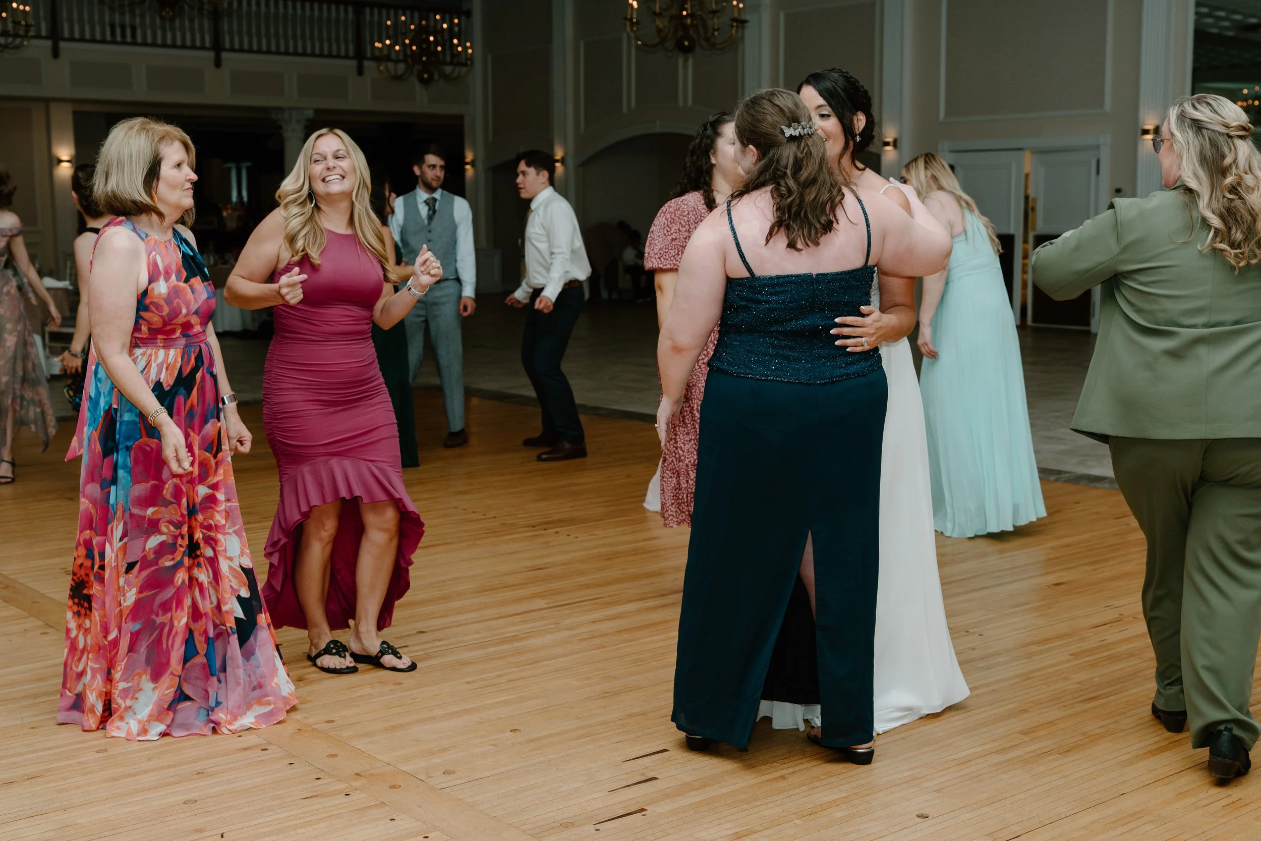 People dancing and socializing at a celebration in a large ballroom, with women in colorful dresses and men in suits during a wedding at the Aqua Turf Club in Connecticut. 