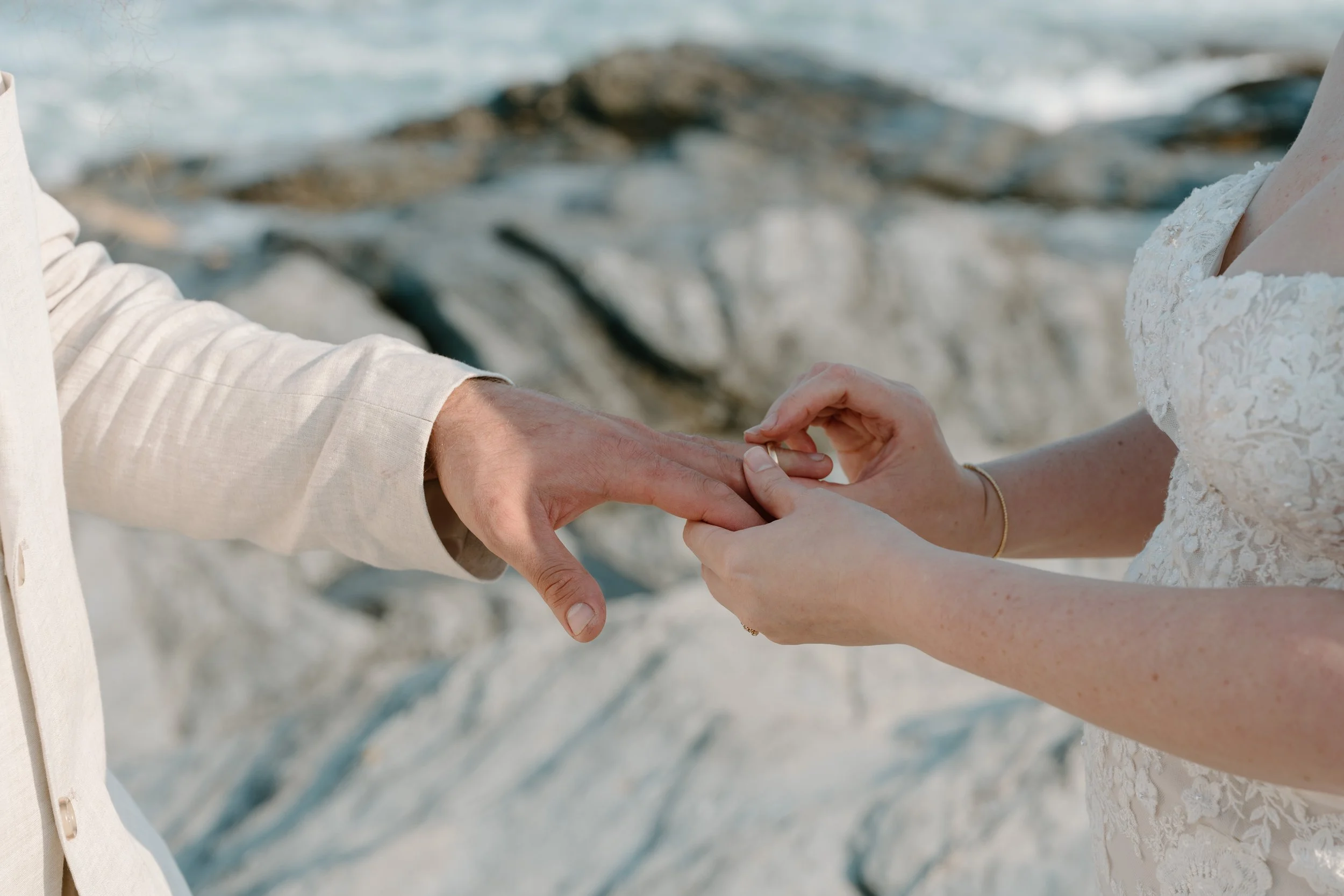 A couple exchanging rings during a wedding ceremony on a rocky beach at an elopement at Beavertail State Park in Rhode Island. 