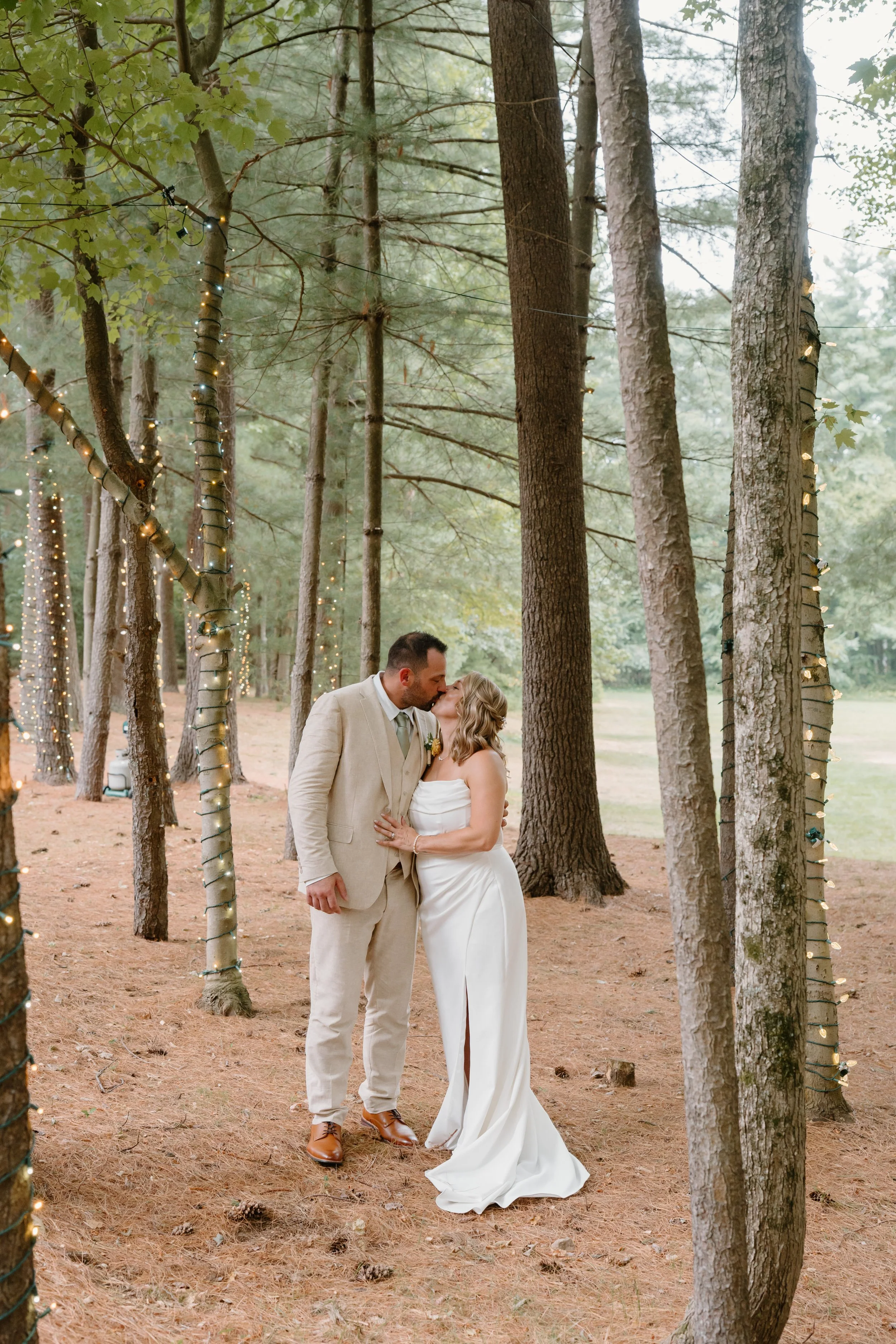 A newlywed couple kissing in a forest decorated with string lights for a wedding at Tunxis Country Club in Connecticut. 