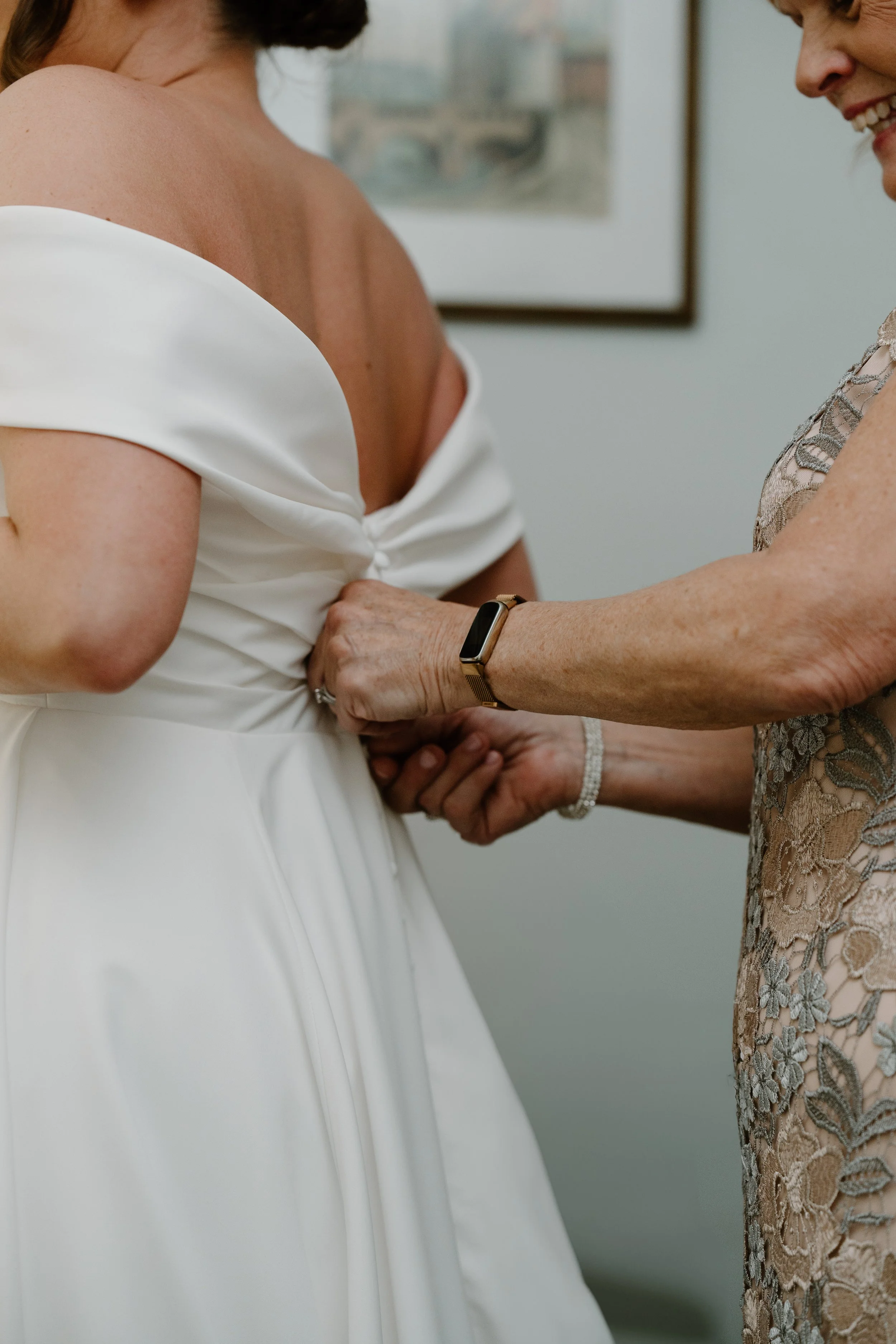 An woman helping a bride with her wedding dress, surrounded by family or friends, indoors for a wedding at Holiday Hill Day Camp in Connecticut.