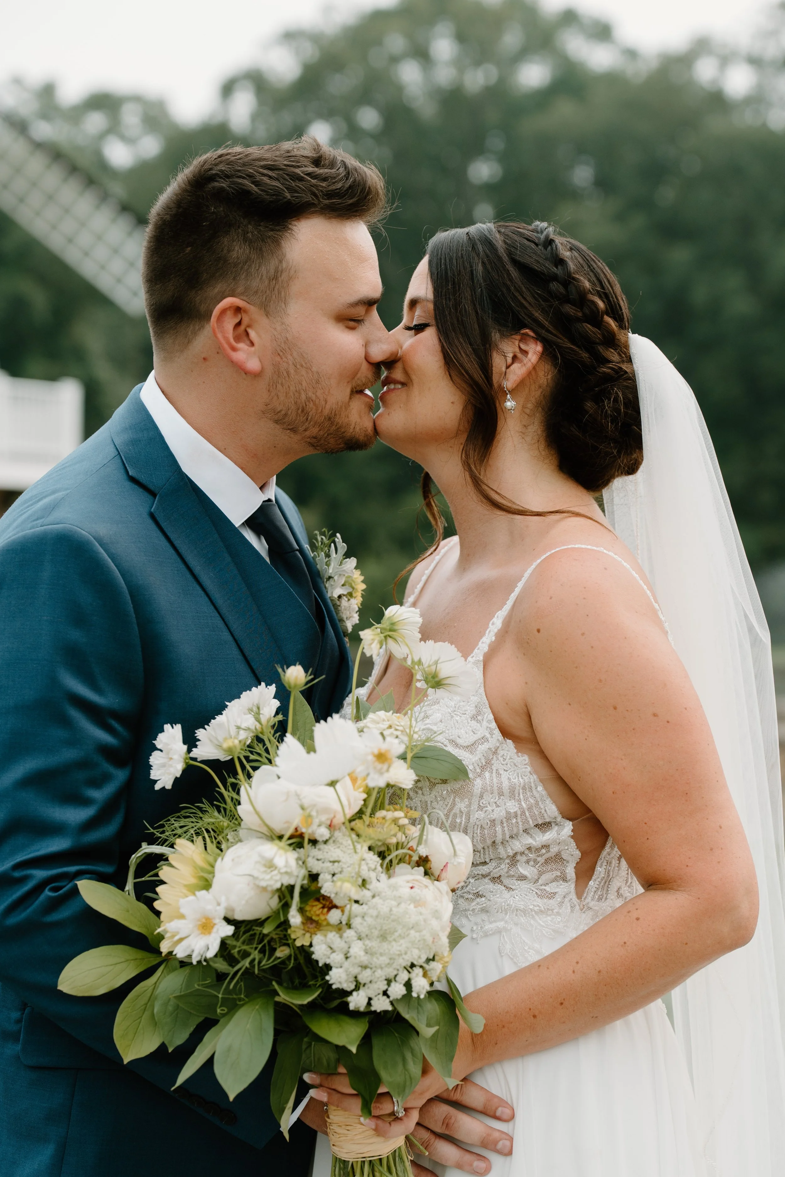 A bride and groom are about to kiss outdoors during their wedding, with greenery and a windmill in the background during a wedding at the Aqua Turf Club in Connecticut. 