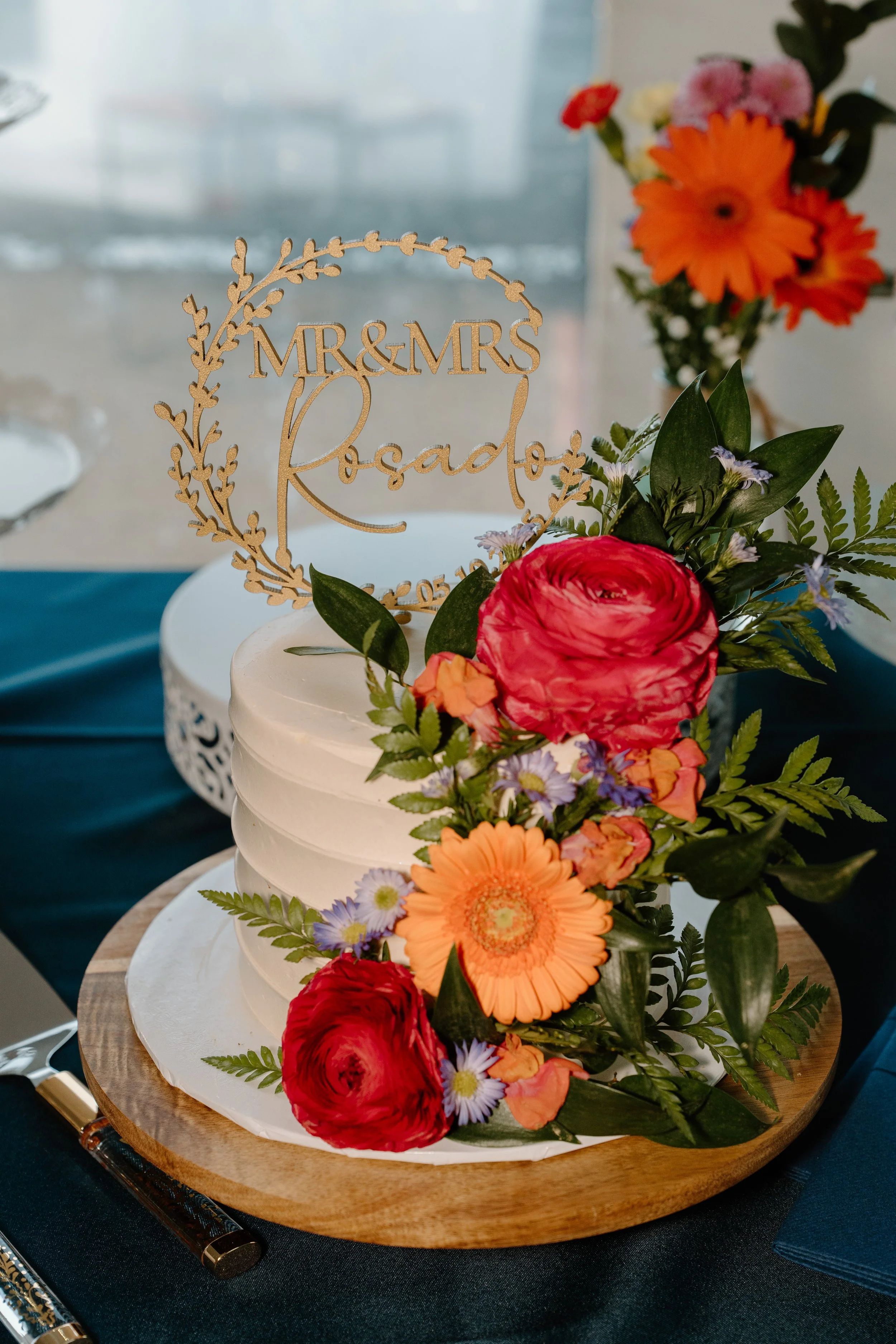 Wedding cake with floral decorations and a topper on a wooden platter for a wedding at Holiday Hill Day Camp in Connecticut.