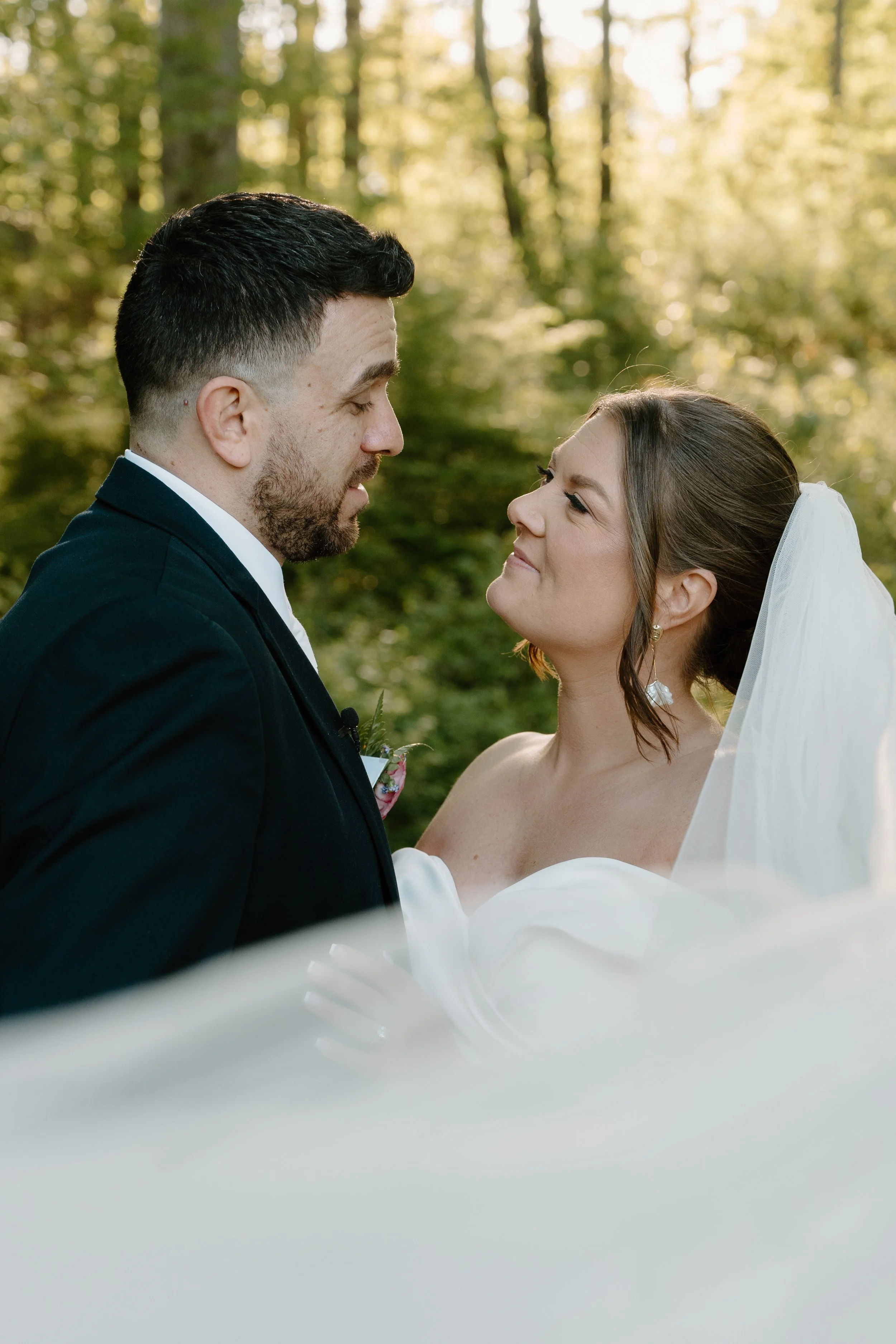 A bride and groom standing close together outdoors in a wooded area, gazing into each other's eyes during sunset for a wedding at Holiday Hill Day Camp in Connecticut.