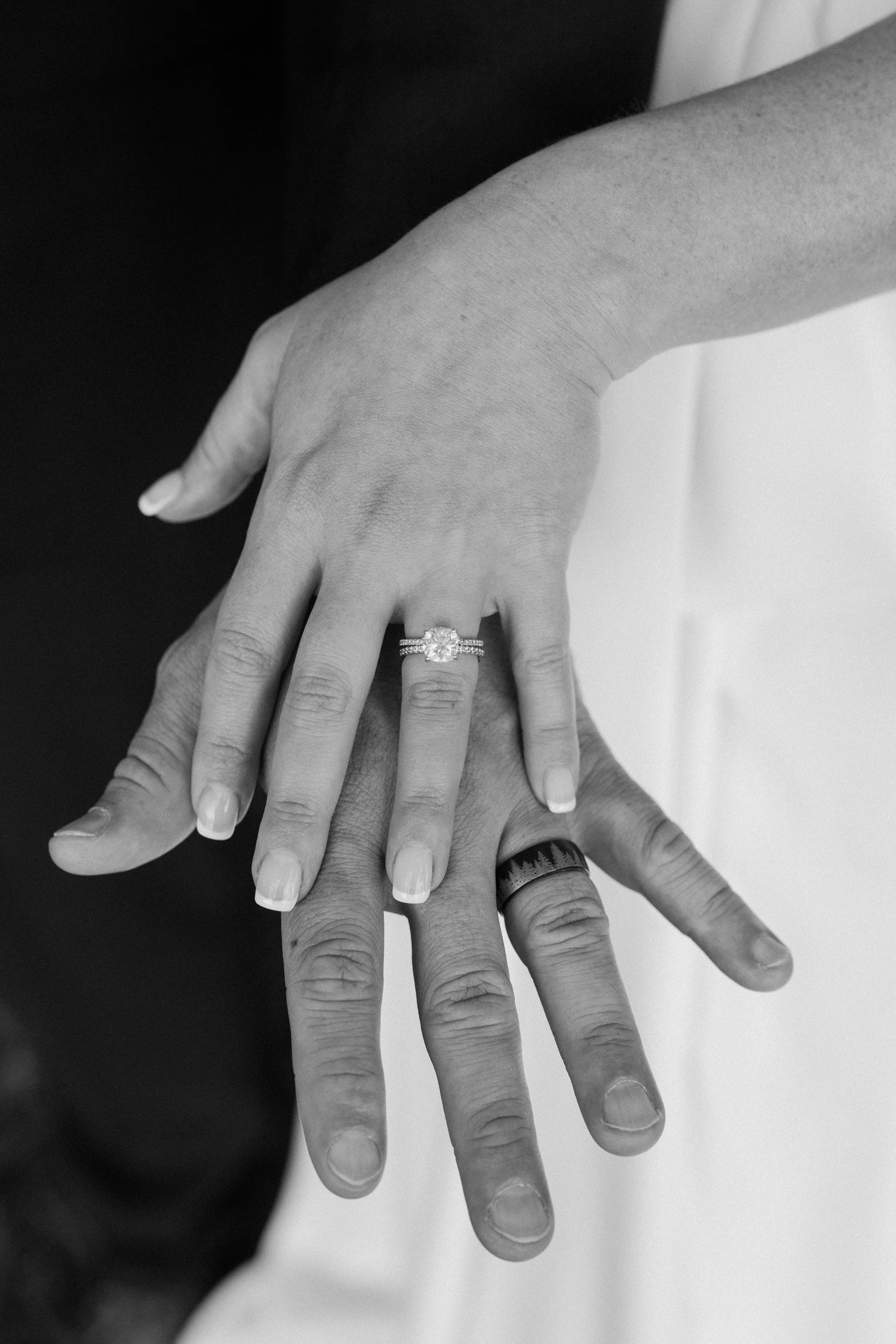 Two hands overlapping, one with an engagement ring and wedding band, the other with a wedding band, black and white photo for a wedding at Holiday Hill Day Camp in Connecticut.