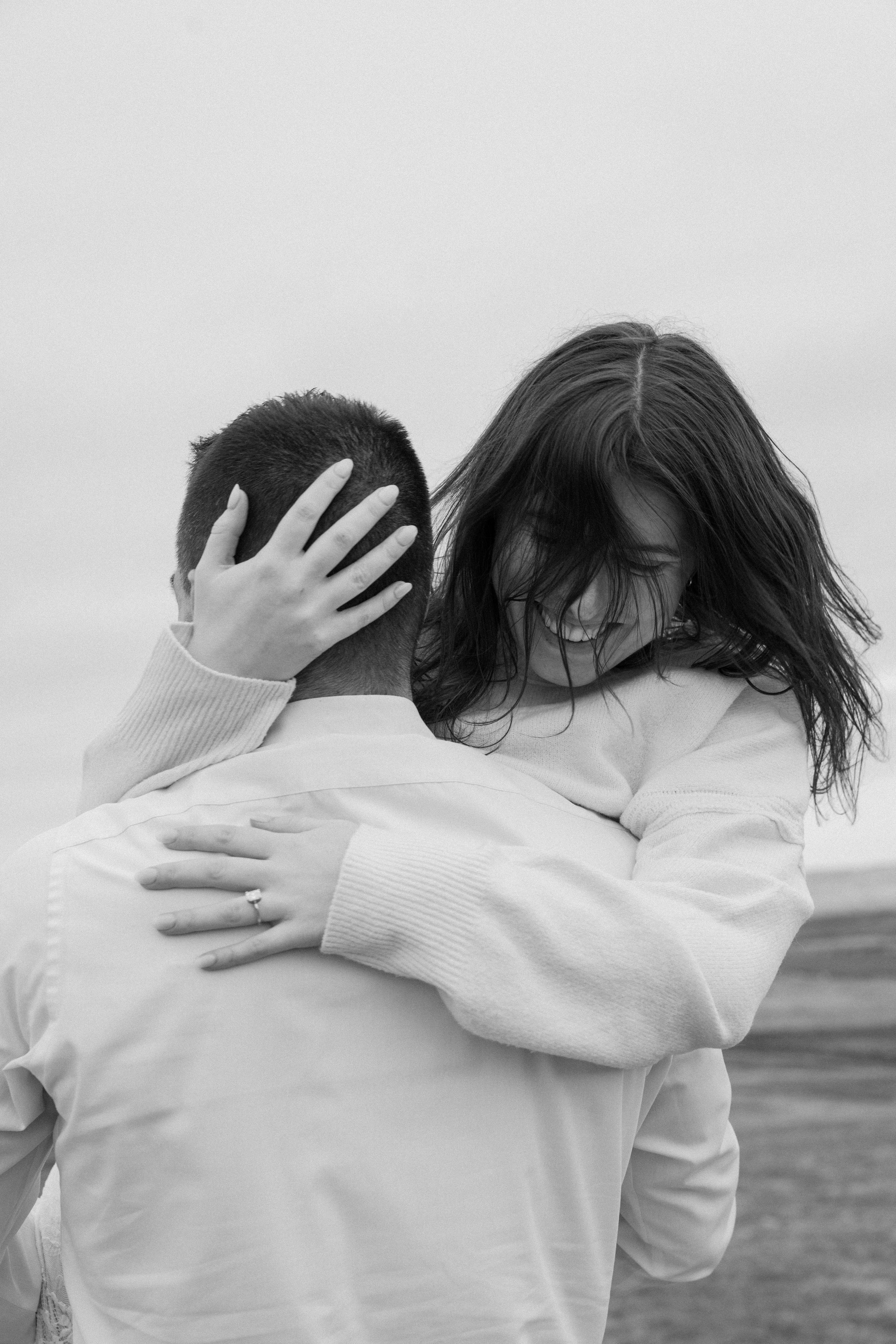 A woman with long hair laughing and hugging a man with short hair outdoors for an engagement photo session in Galway, Ireland. 