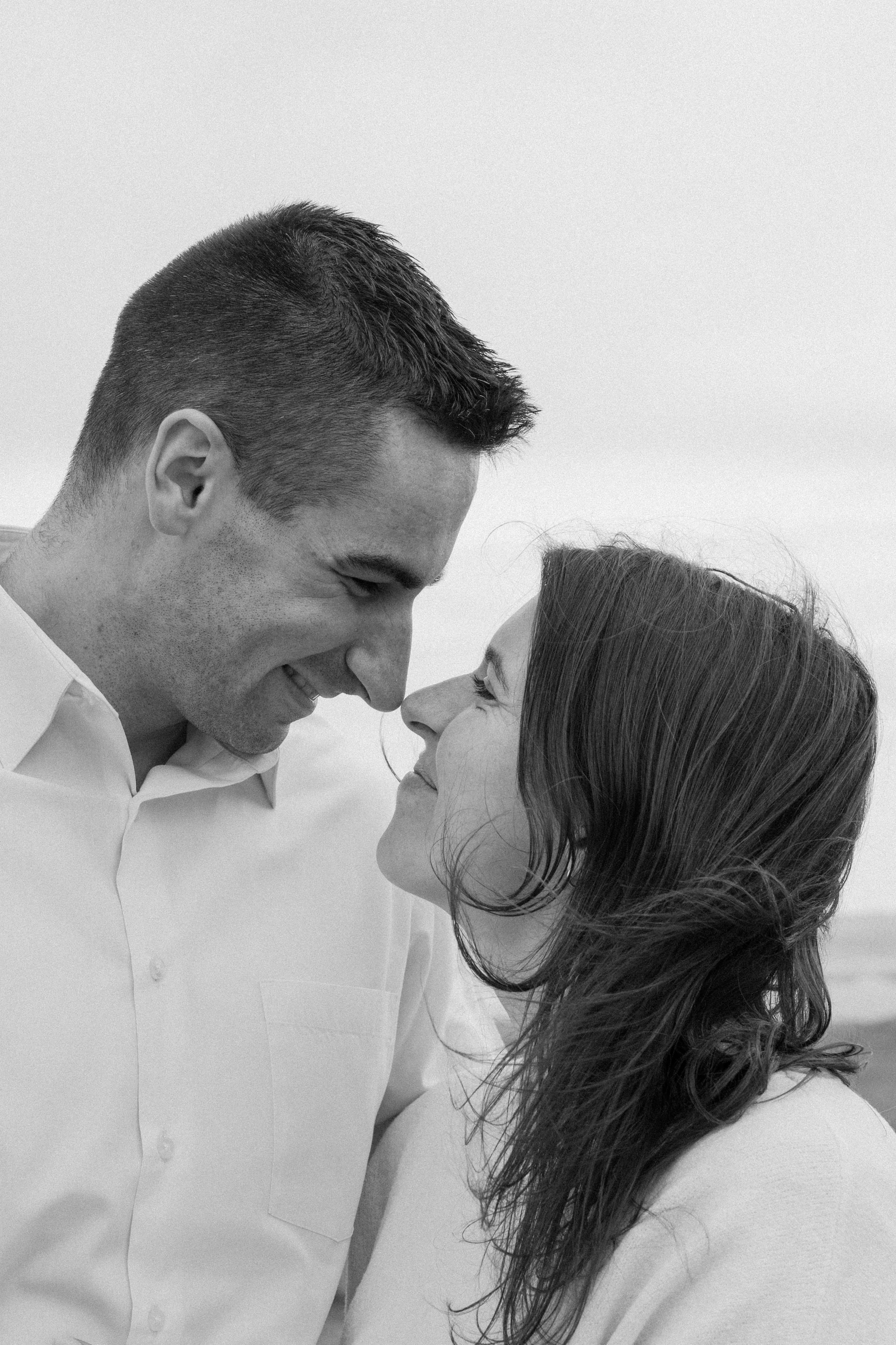 A black and white photo of a man and woman smiling and touching noses outdoors for an engagement photo session in Galway, Ireland. 