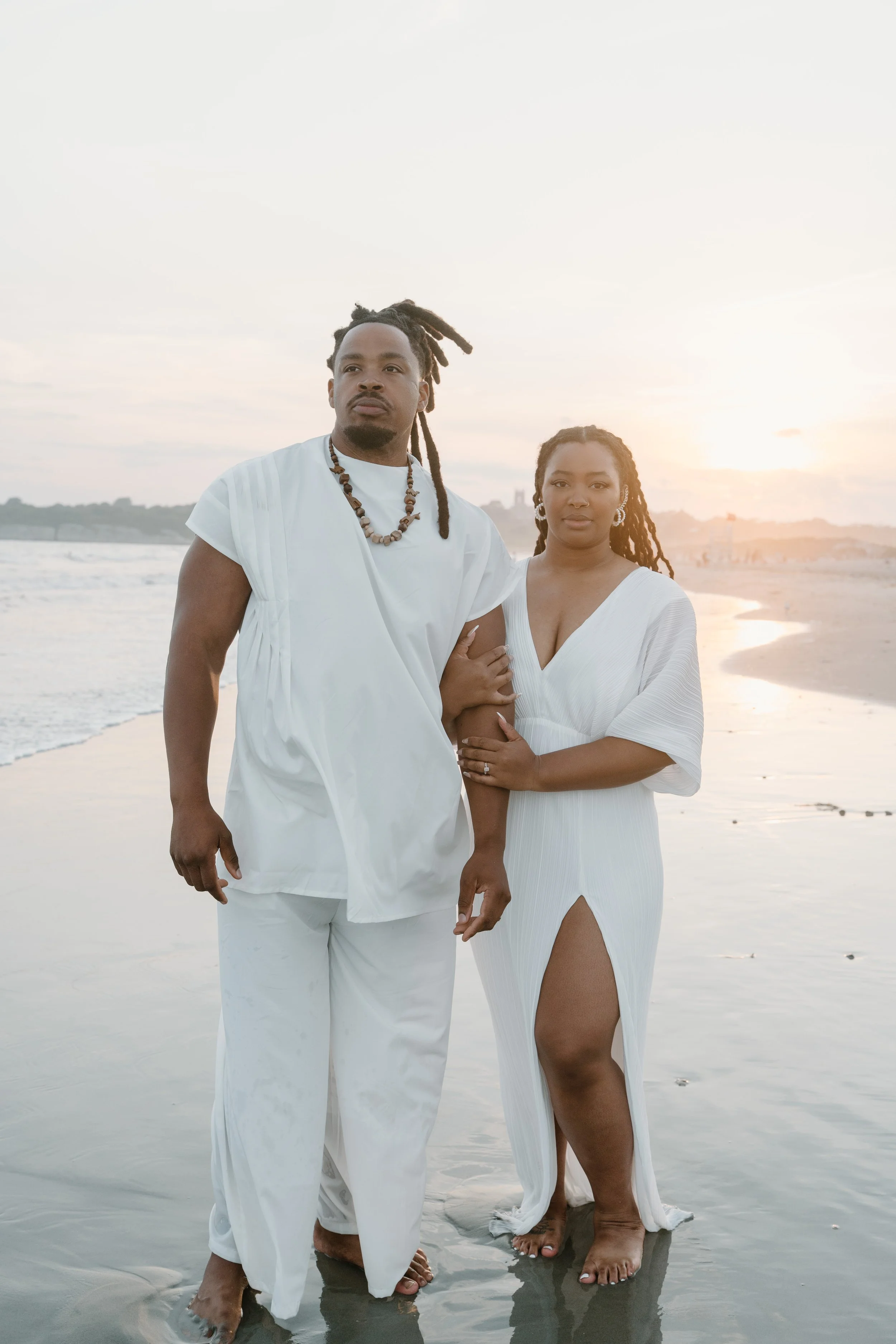 A couple dressed in white standing on the beach at sunset, holding hands at an elopement at Second Beach in Rhode Island. 